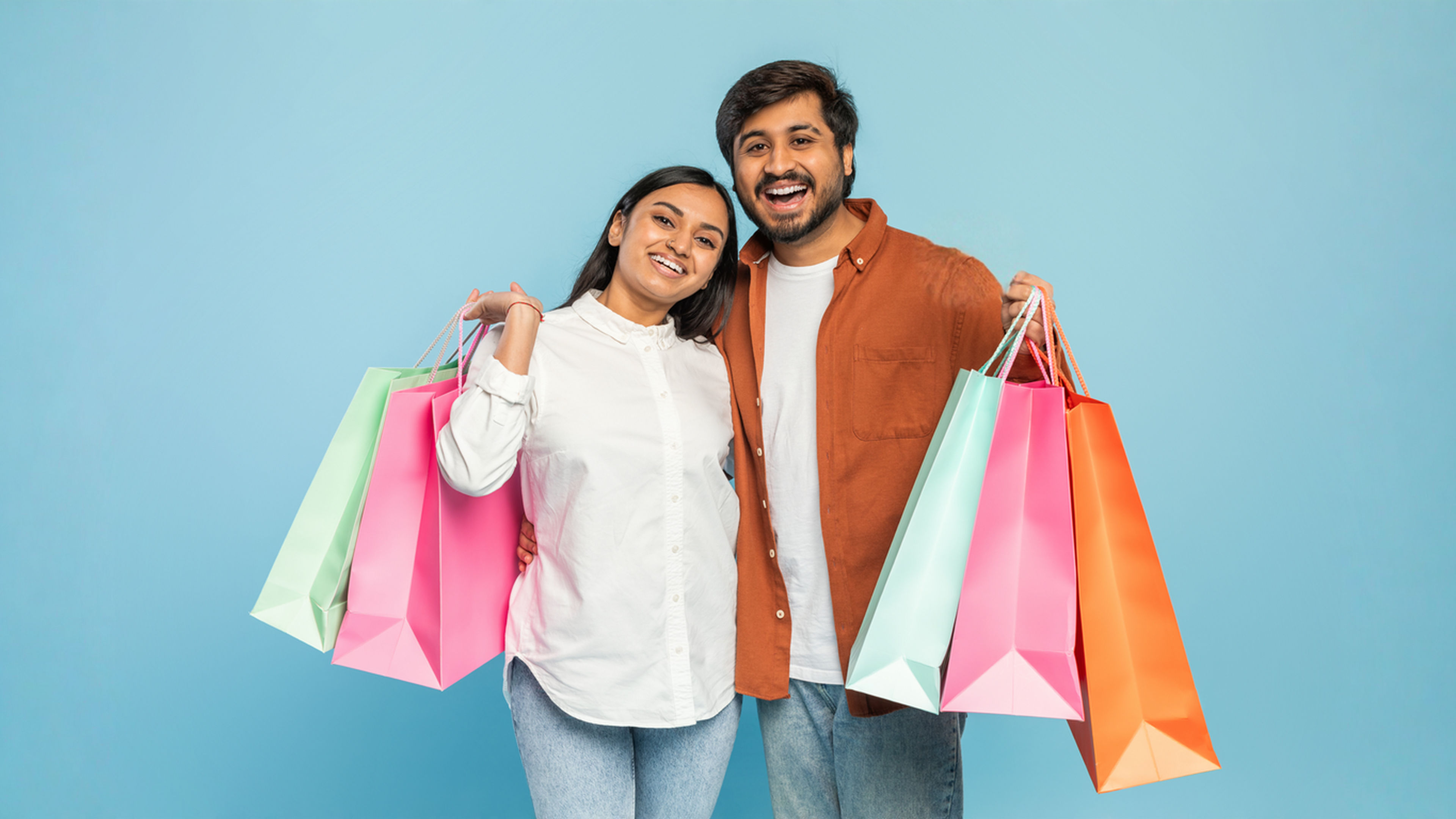 Couple with shopping bags looking joyful on blue background.