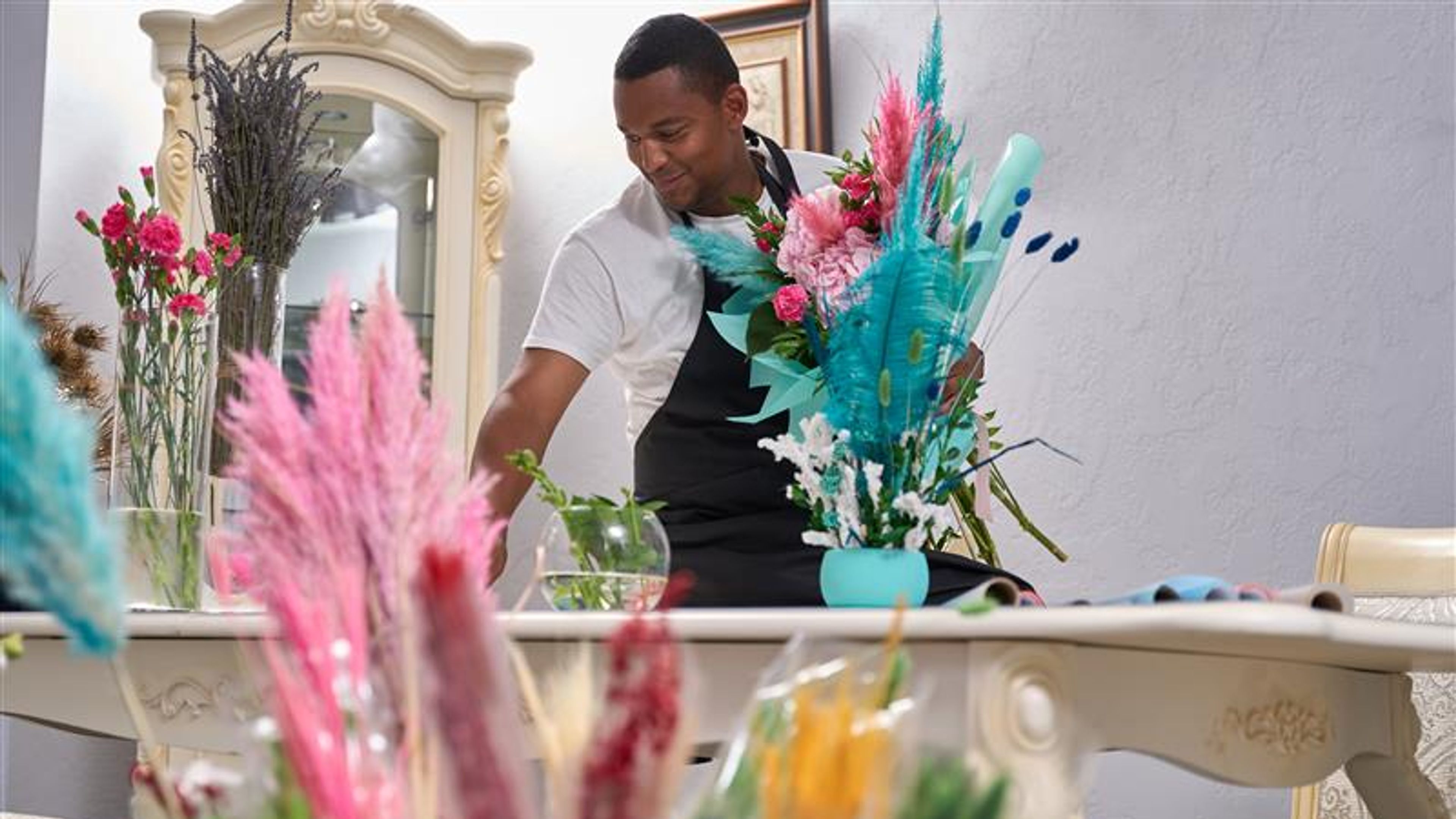 A cheerful florist is holding a fresh bouquet while standing in front of a decorated table.