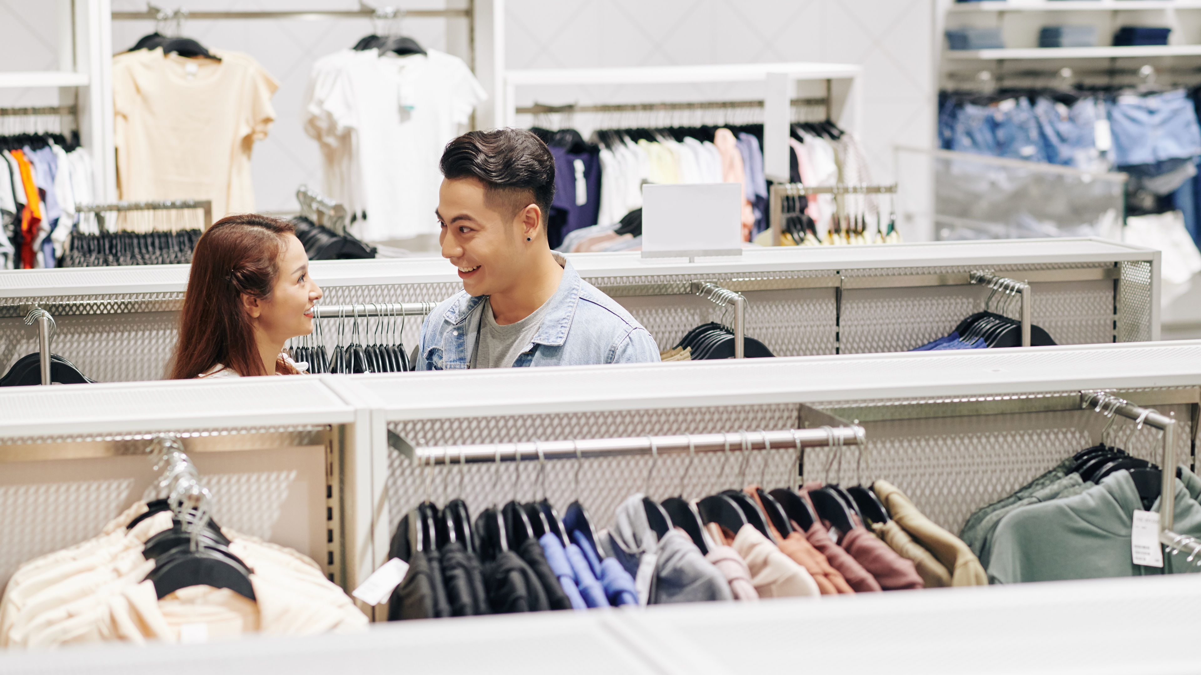 Nakangiting mag asawa na namimili ng mga damit sa isang tindahan, nagba browse sa mga rack ng damit.