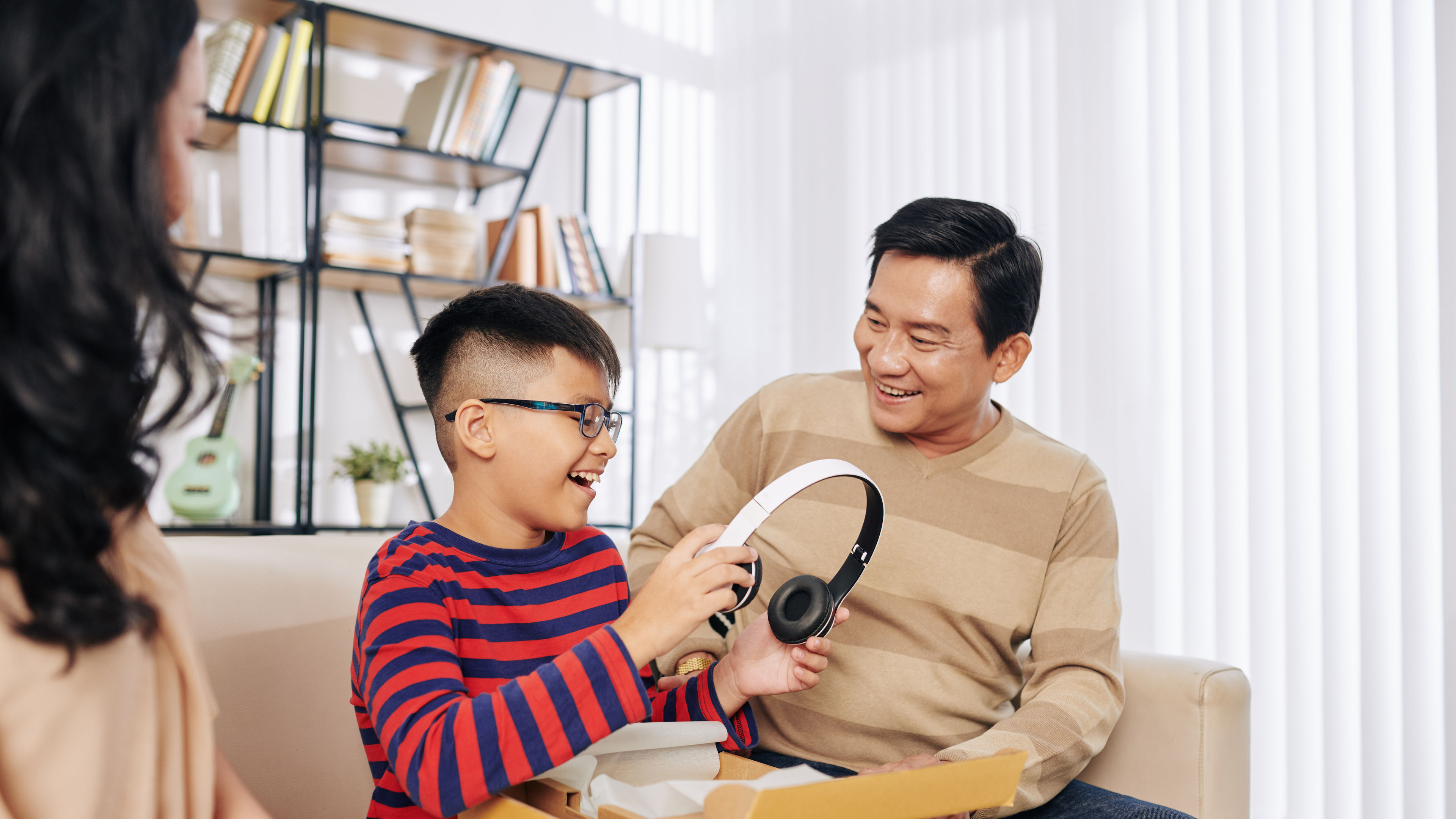 A boy opening a box of earphones with his parents