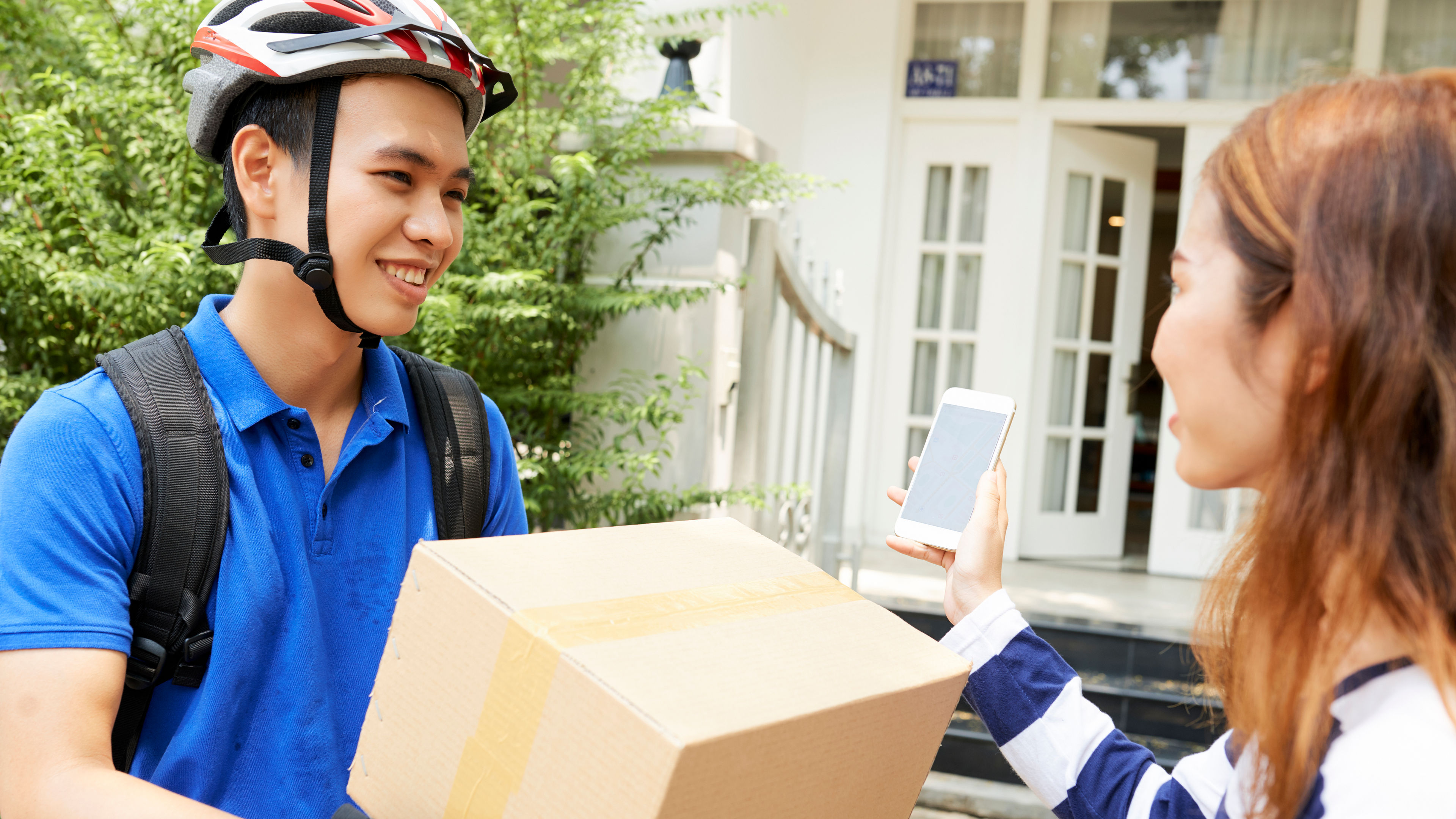 A happy delivery man delivering a carton to a woman 