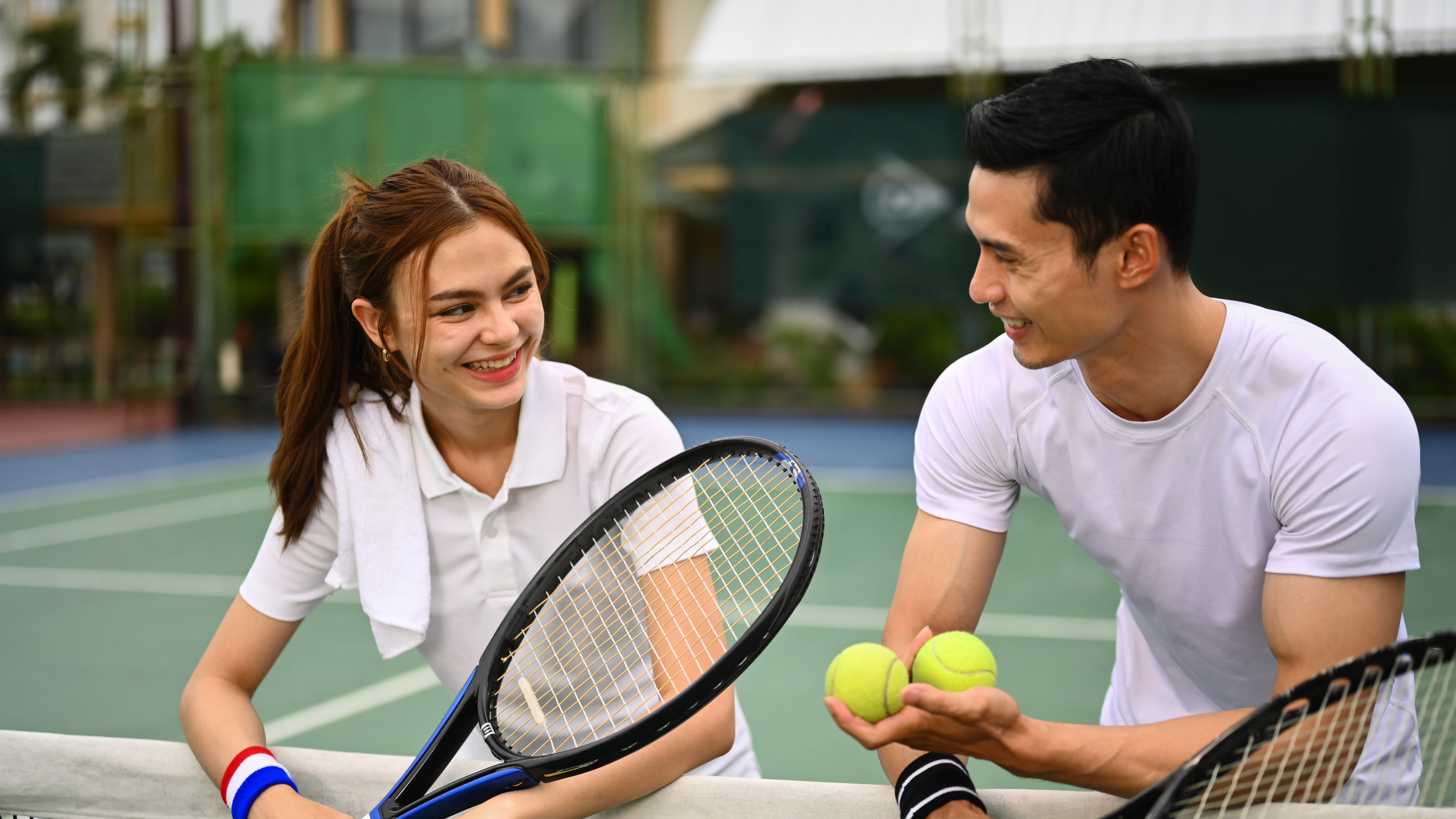 Asian tennis players smiling and chatting on the court. 