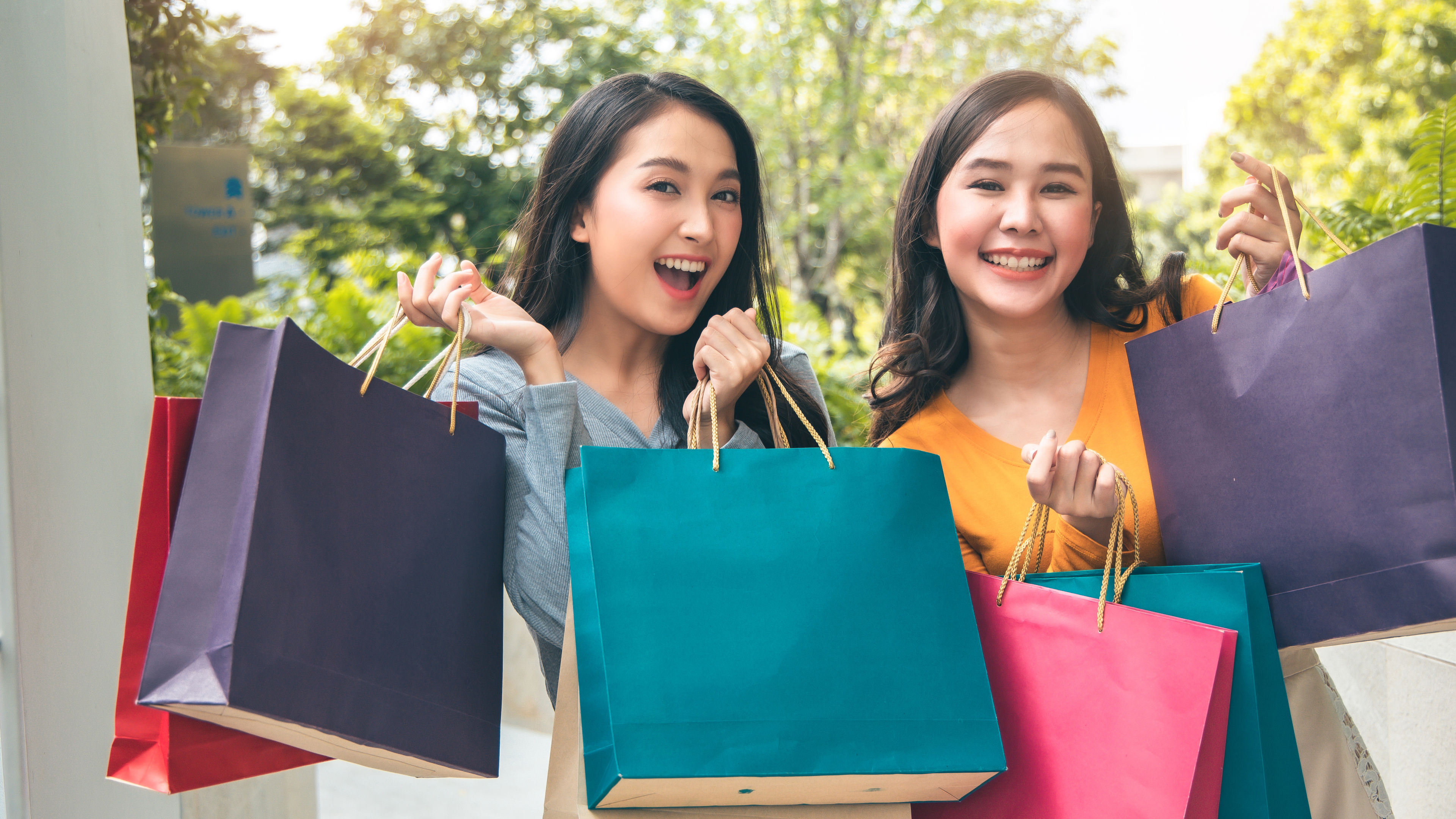 Malaysian female friends smiling and posing with shopping bags in hand
