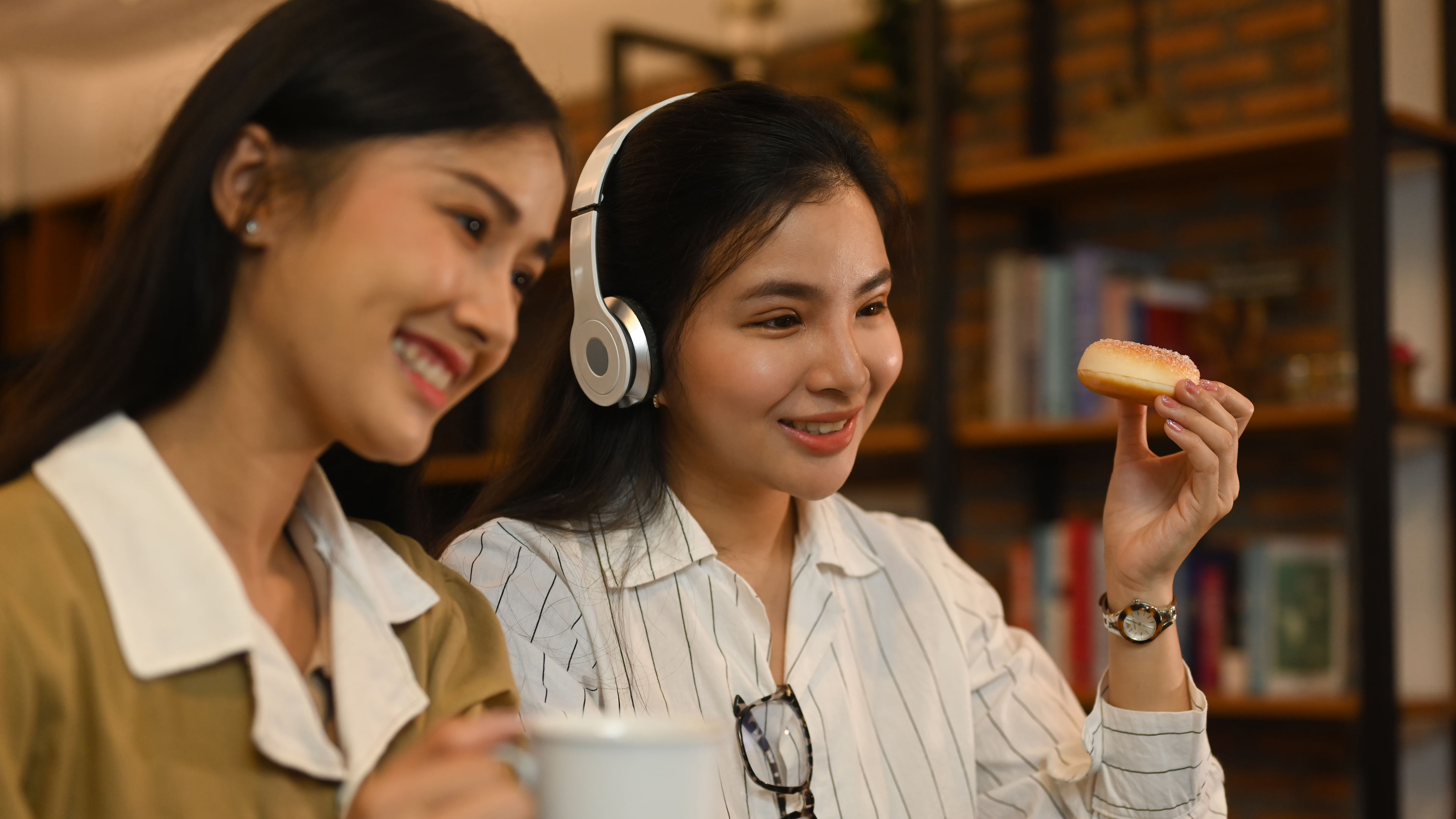 Dalawang magkaibigan na nagpapahinga sa isang coffee shop, na nasisiyahan sa meryenda at musika.