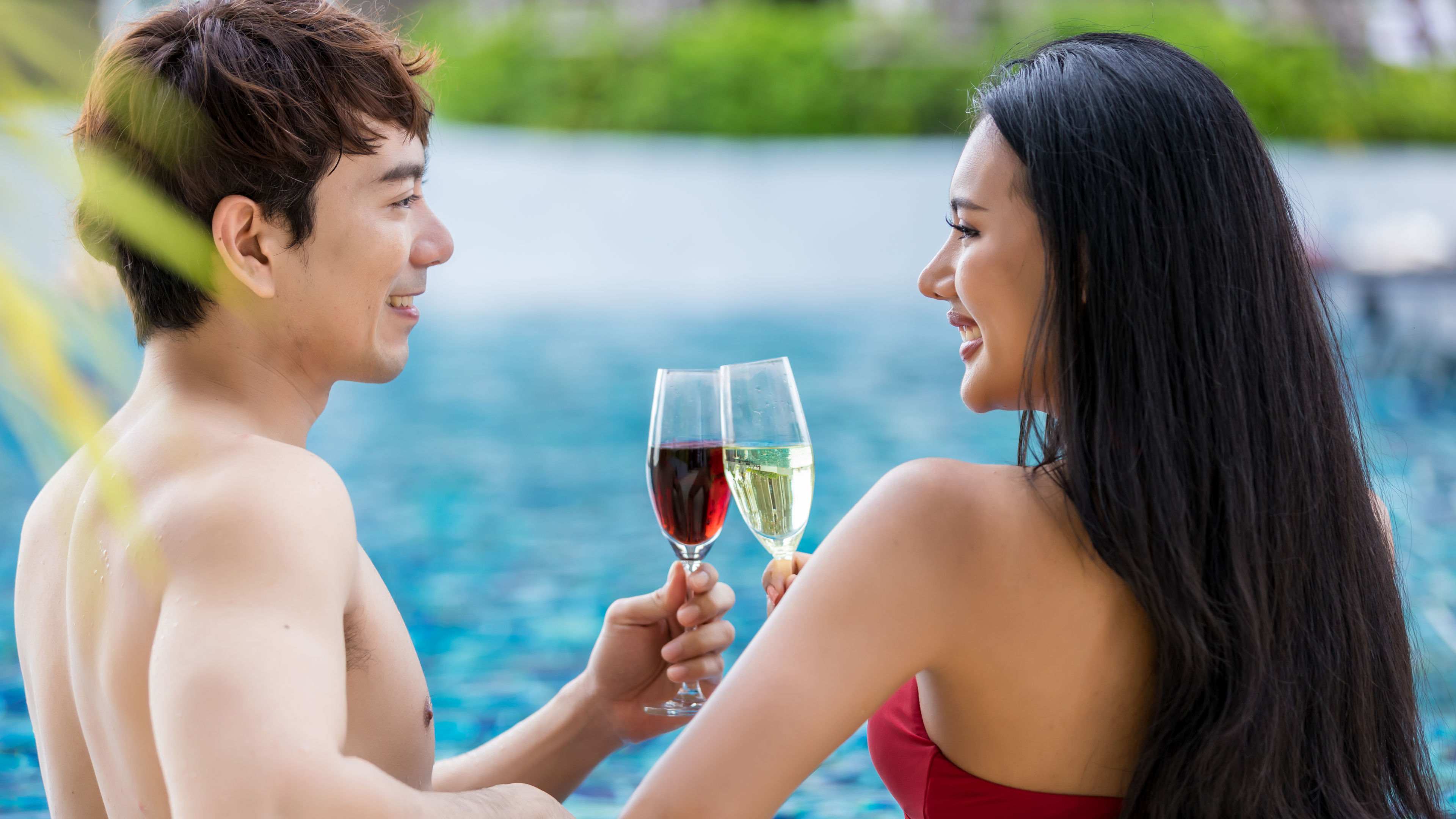 Young Asian lovers with red and golden champagne on pool