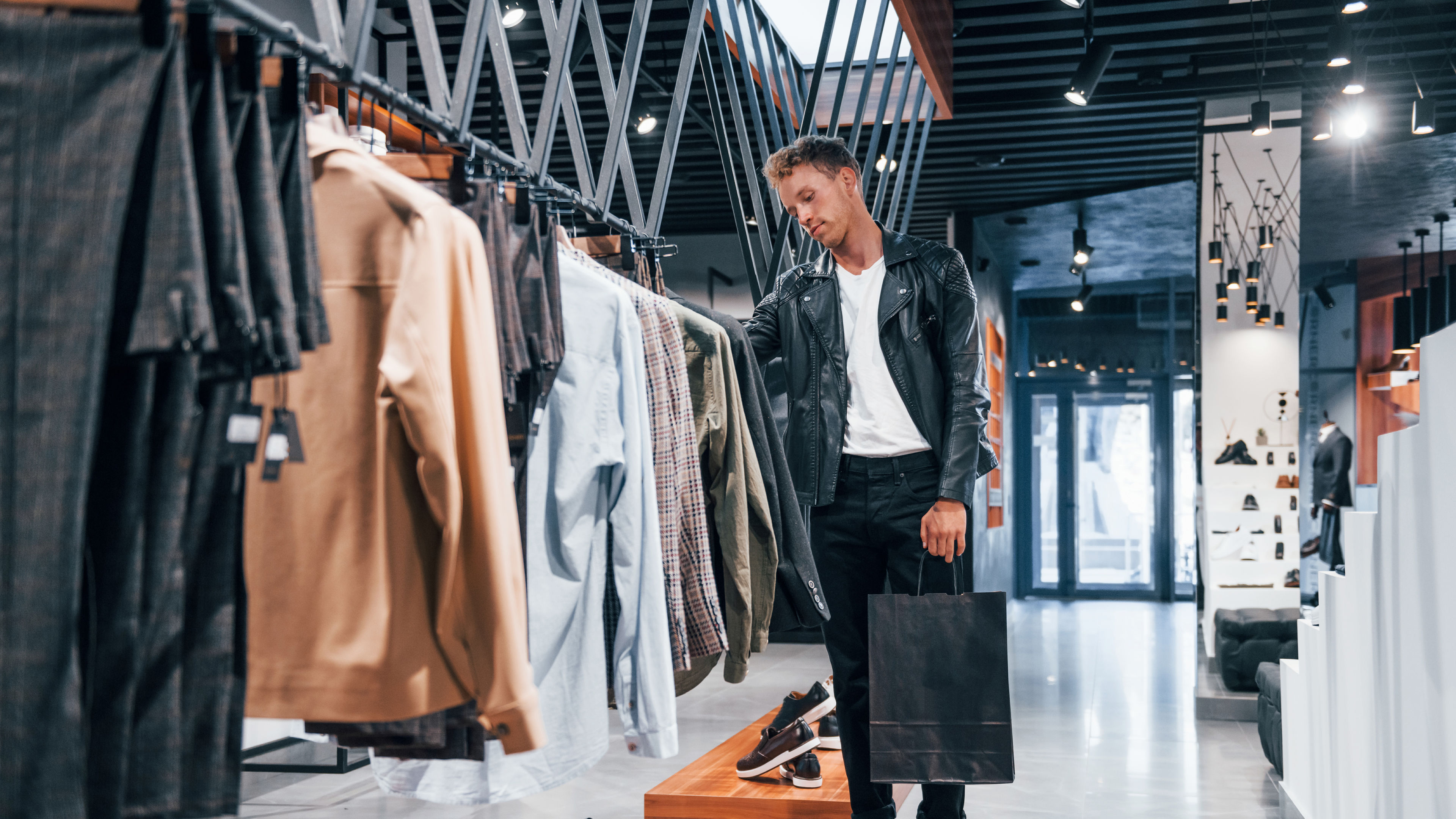 Young guy in modern store checking new clothes on rack.