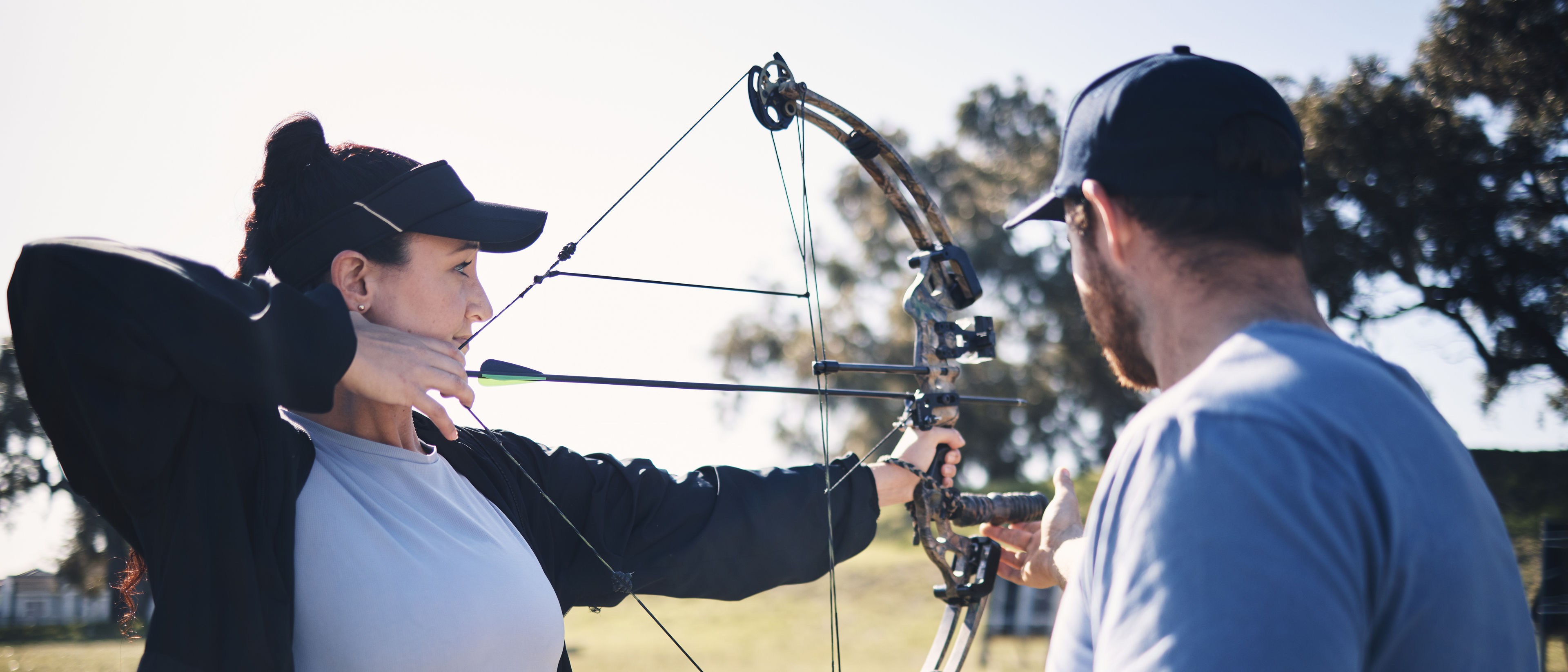 A woman aims her bow and arrow at a target with the guidance of her coach.