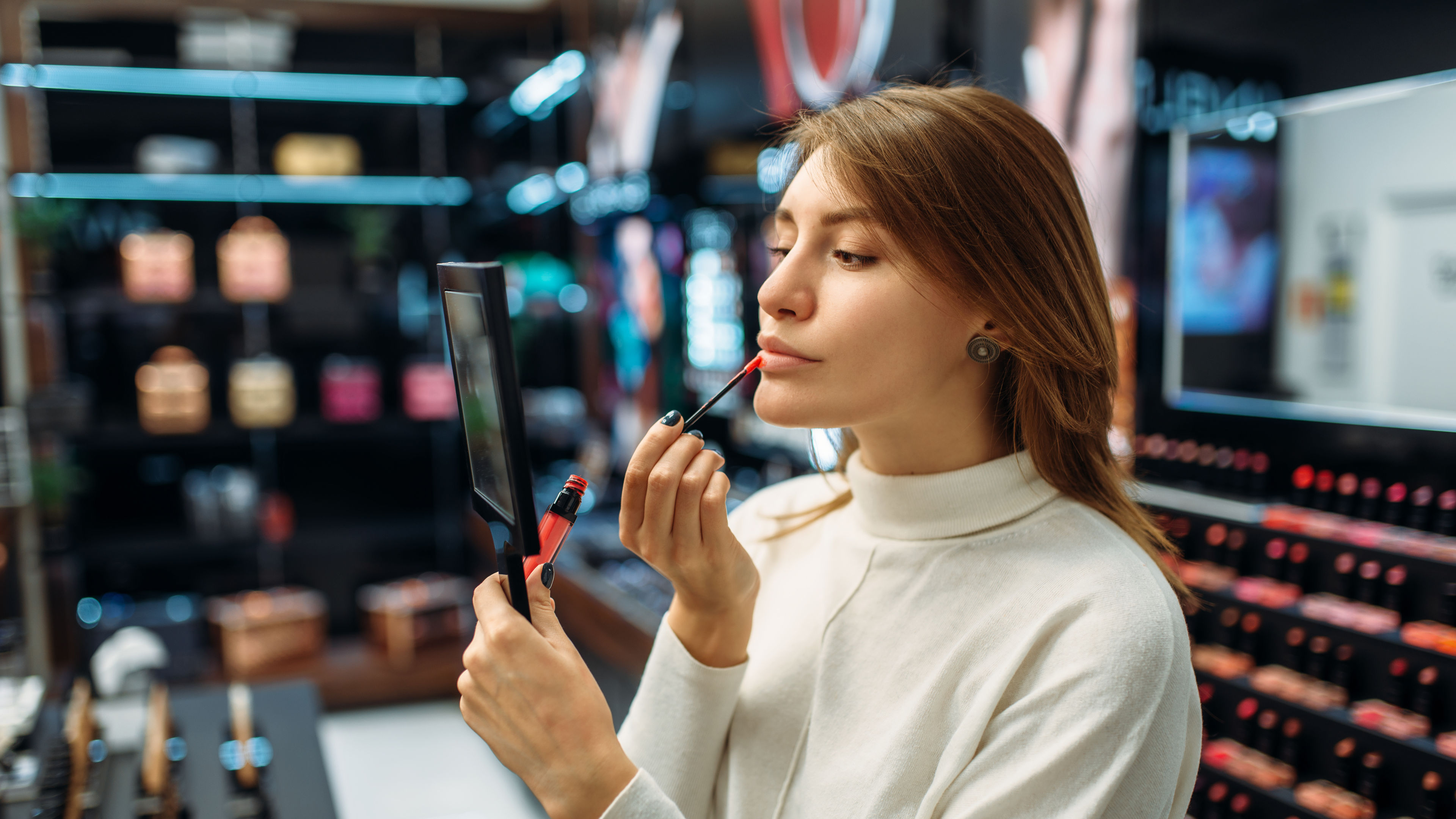Female customer testing lip liner in a makeup shop, looking in a mirror