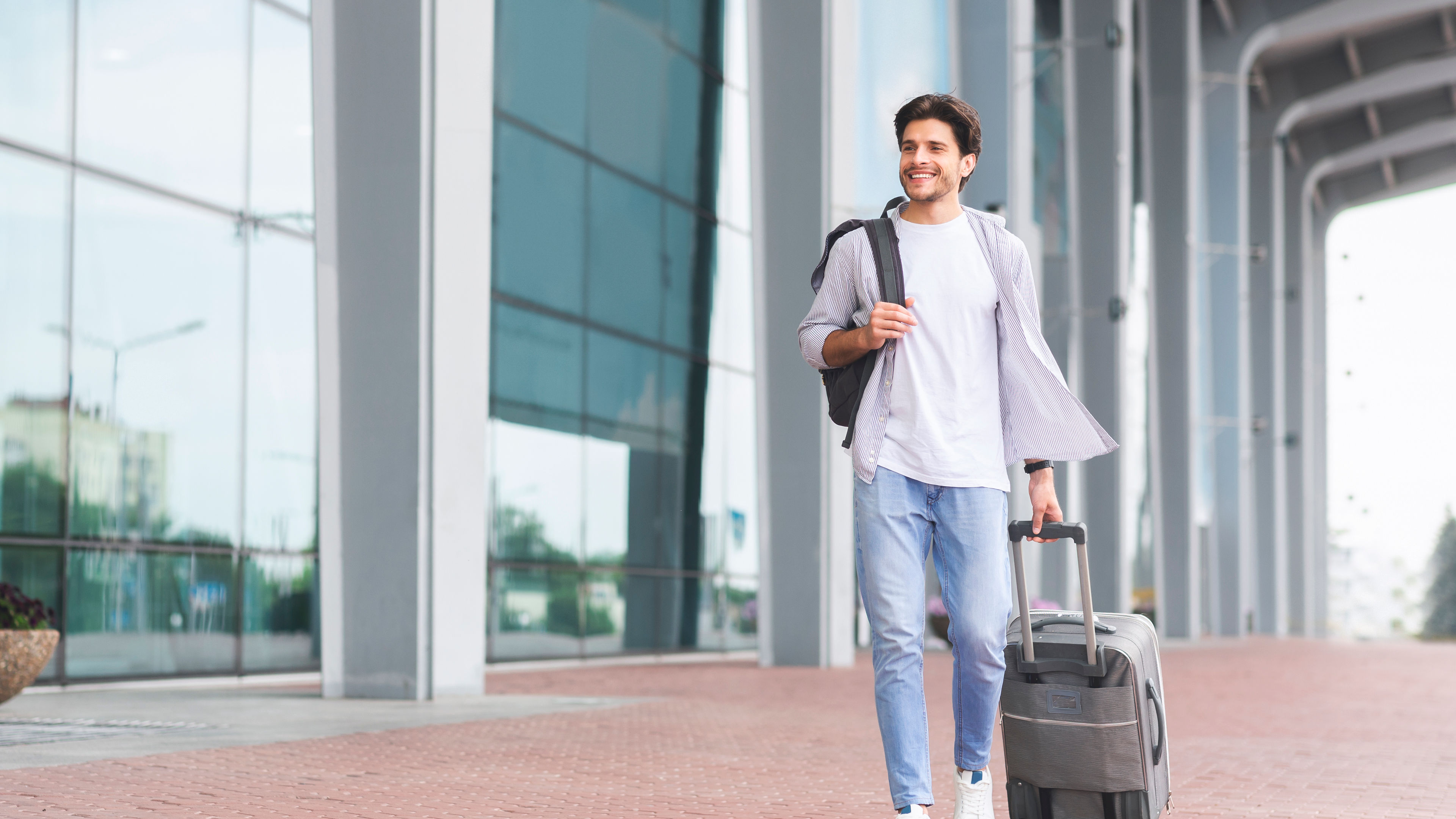 A happy man is walking with a suitcase. 
