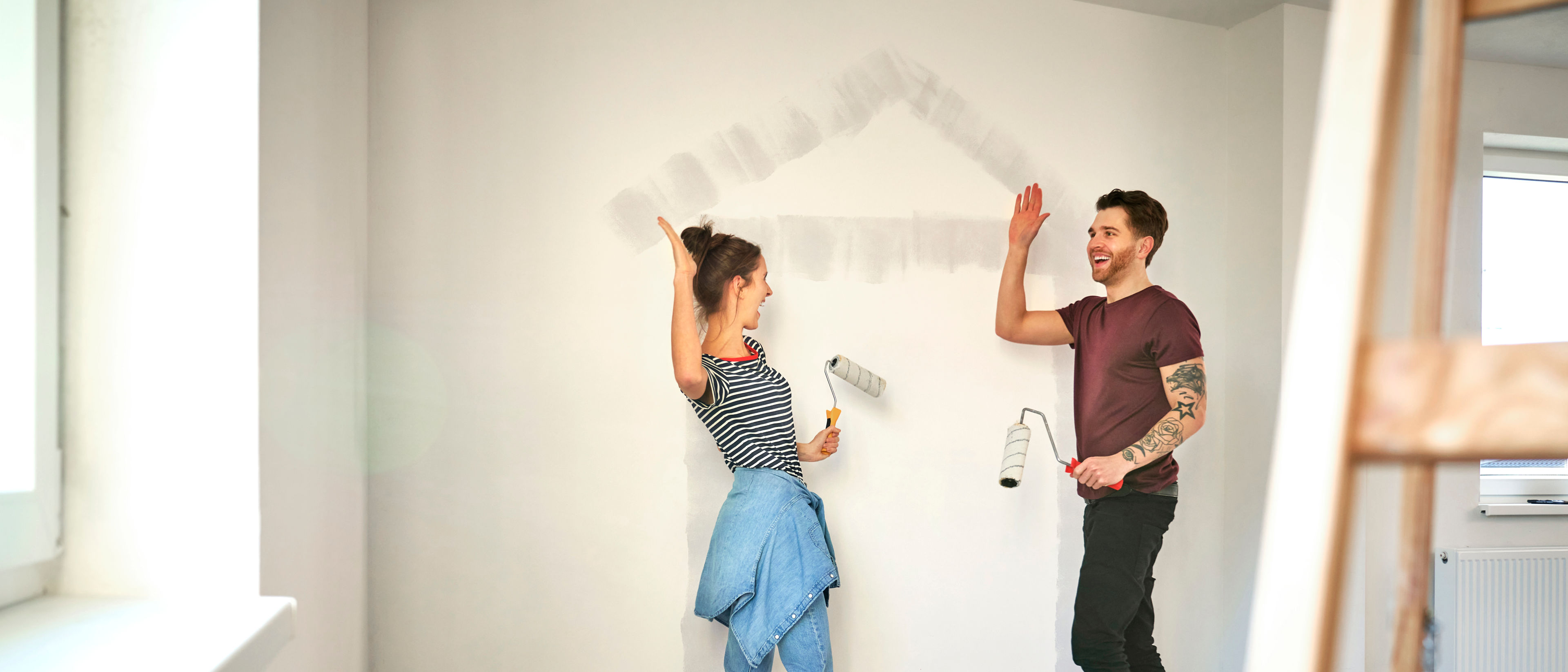 A young couple shares a high five, smiling and celebrating after finishing the task of painting a house-shaped design.