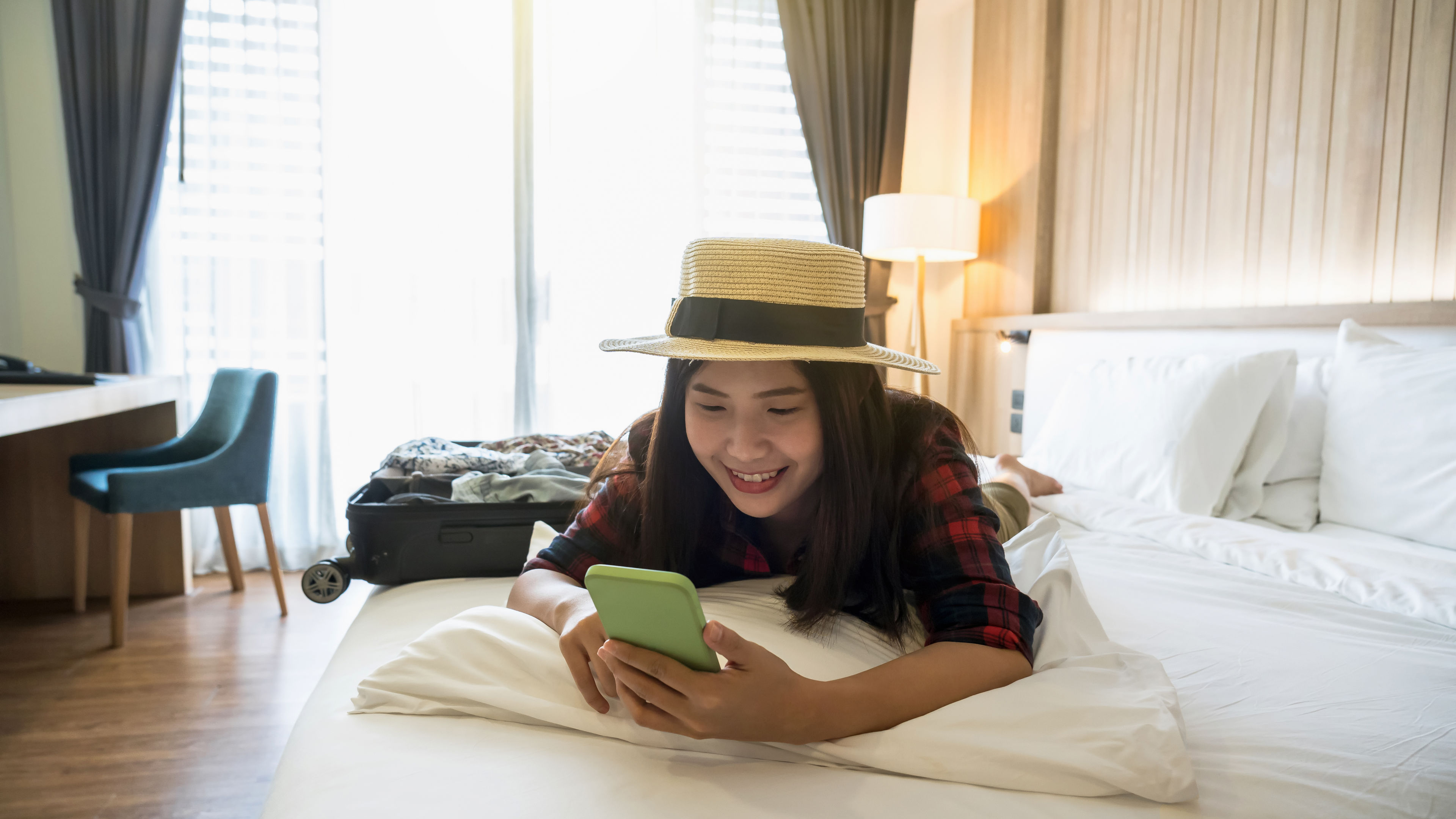 Happy Asian traveler woman sleeping and using the smart mobile phone on the bed.