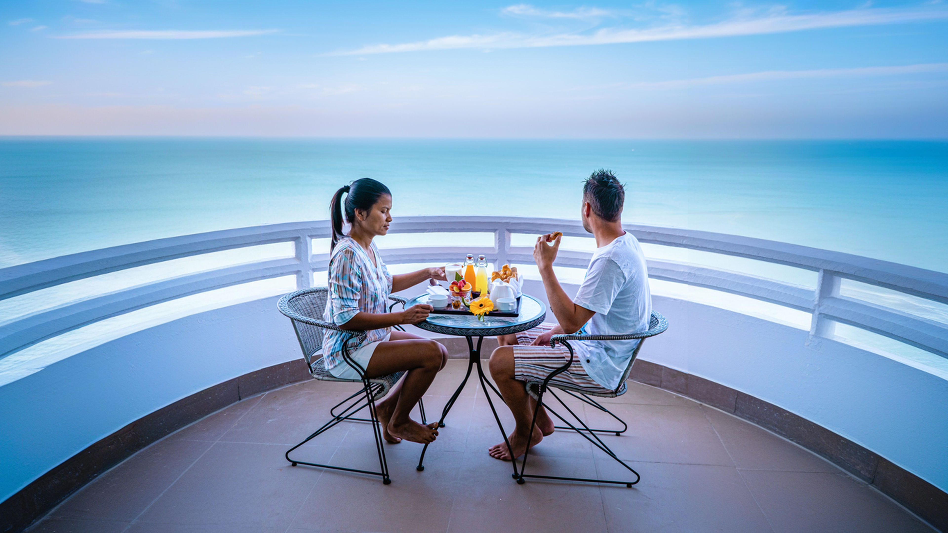 Couple having breakfast on balcony looking out over the ocean on vacation.
