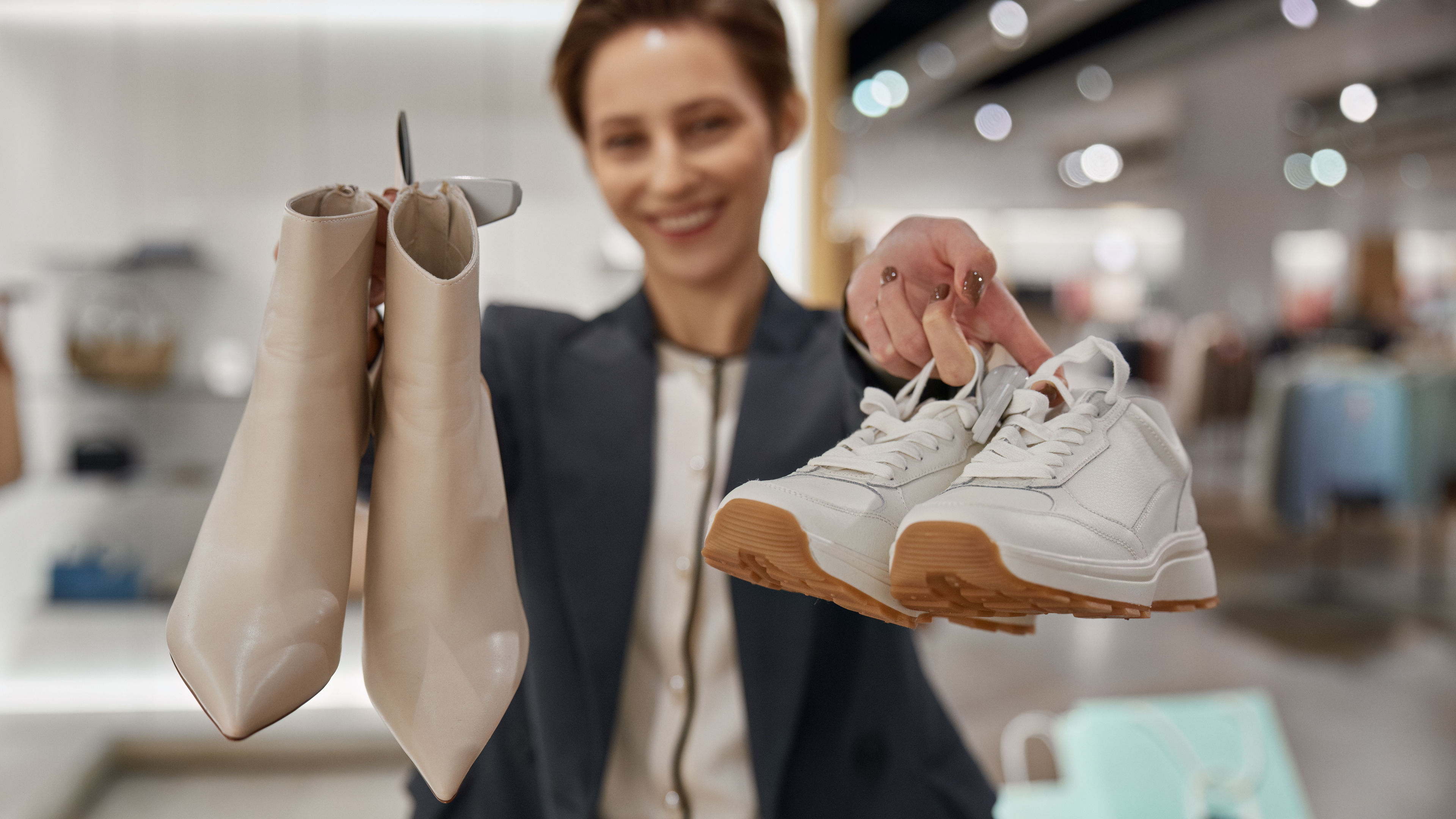 A smiling Asian woman with nail polish is holding two pairs of stylish shoes.