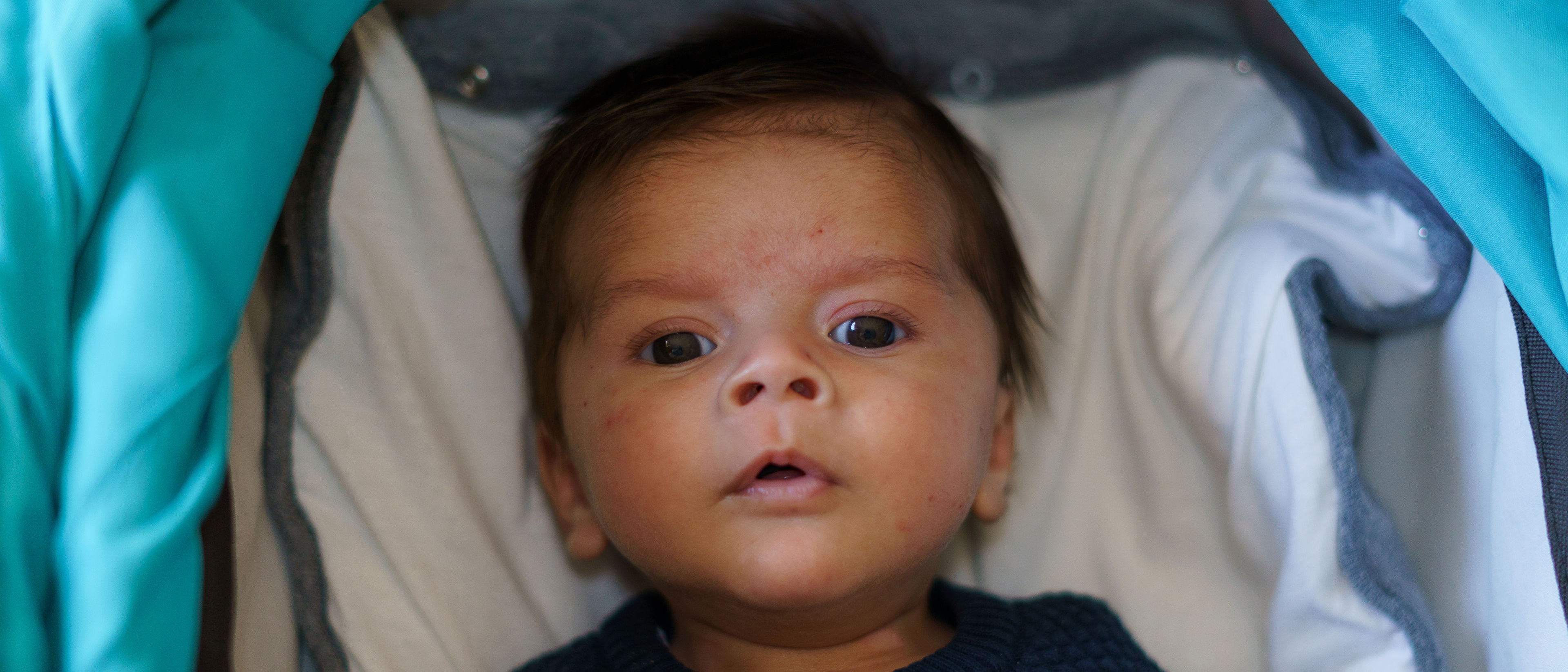 A newborn baby lies quietly in a cradle, wrapped in a soft blanket