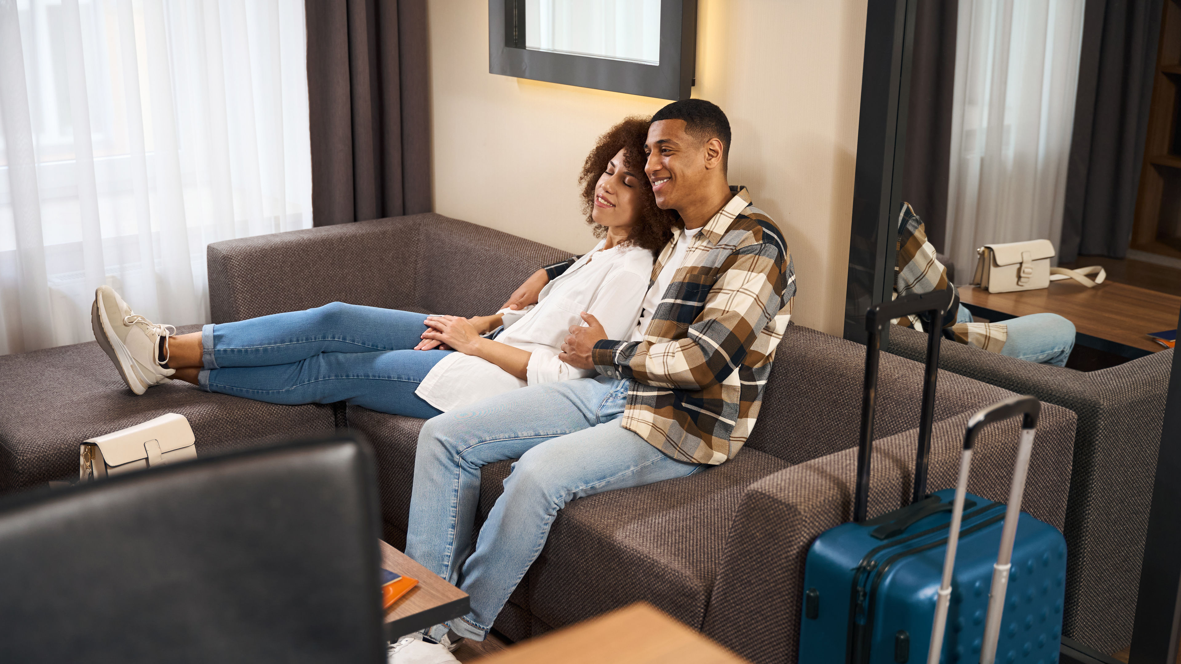 A happy couple relaxing on a hotel sofa with luggage nearby.