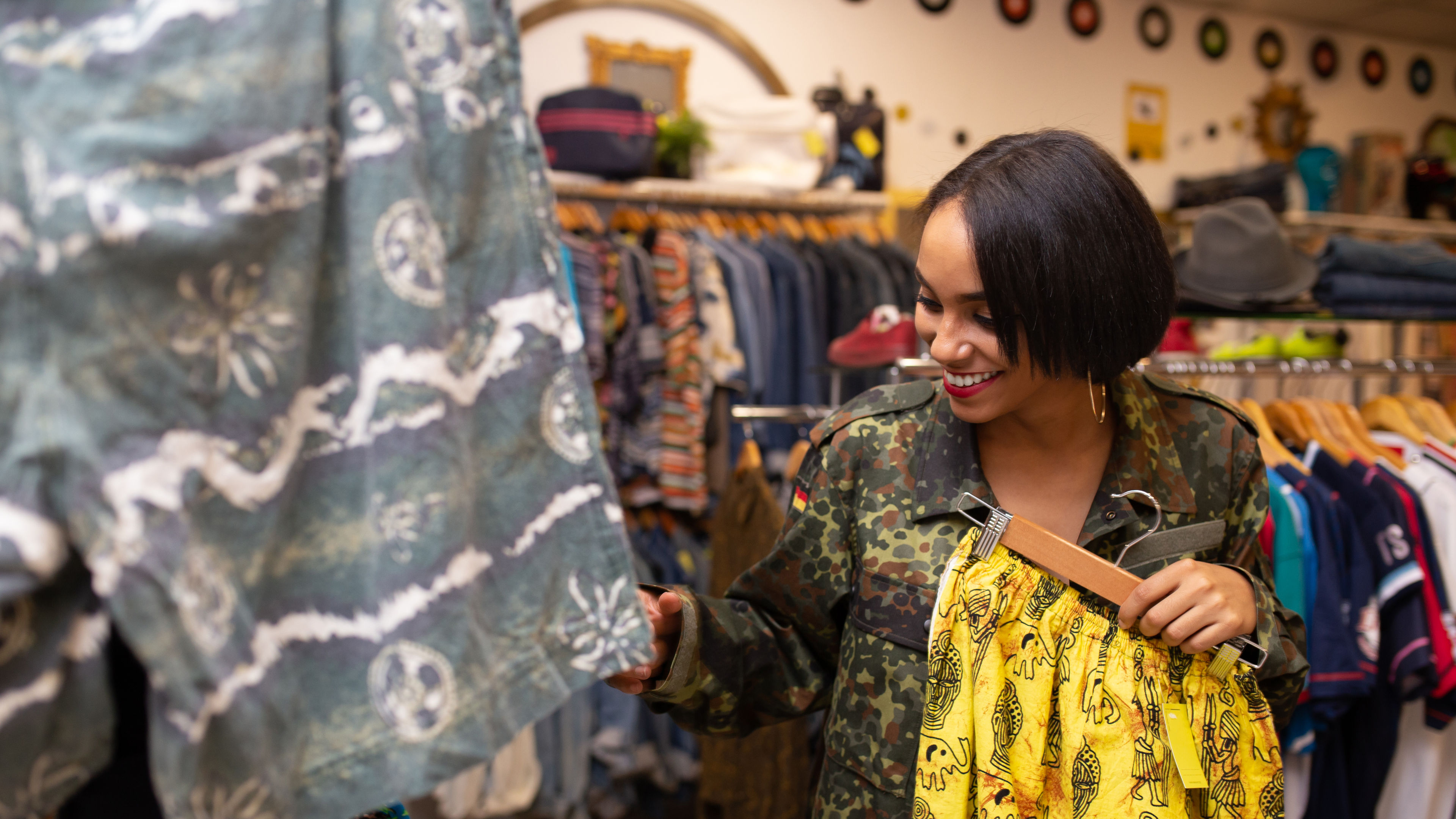 A young woman browsing clothes on a rail, holding a yellow dress in her hand, inside a shop.