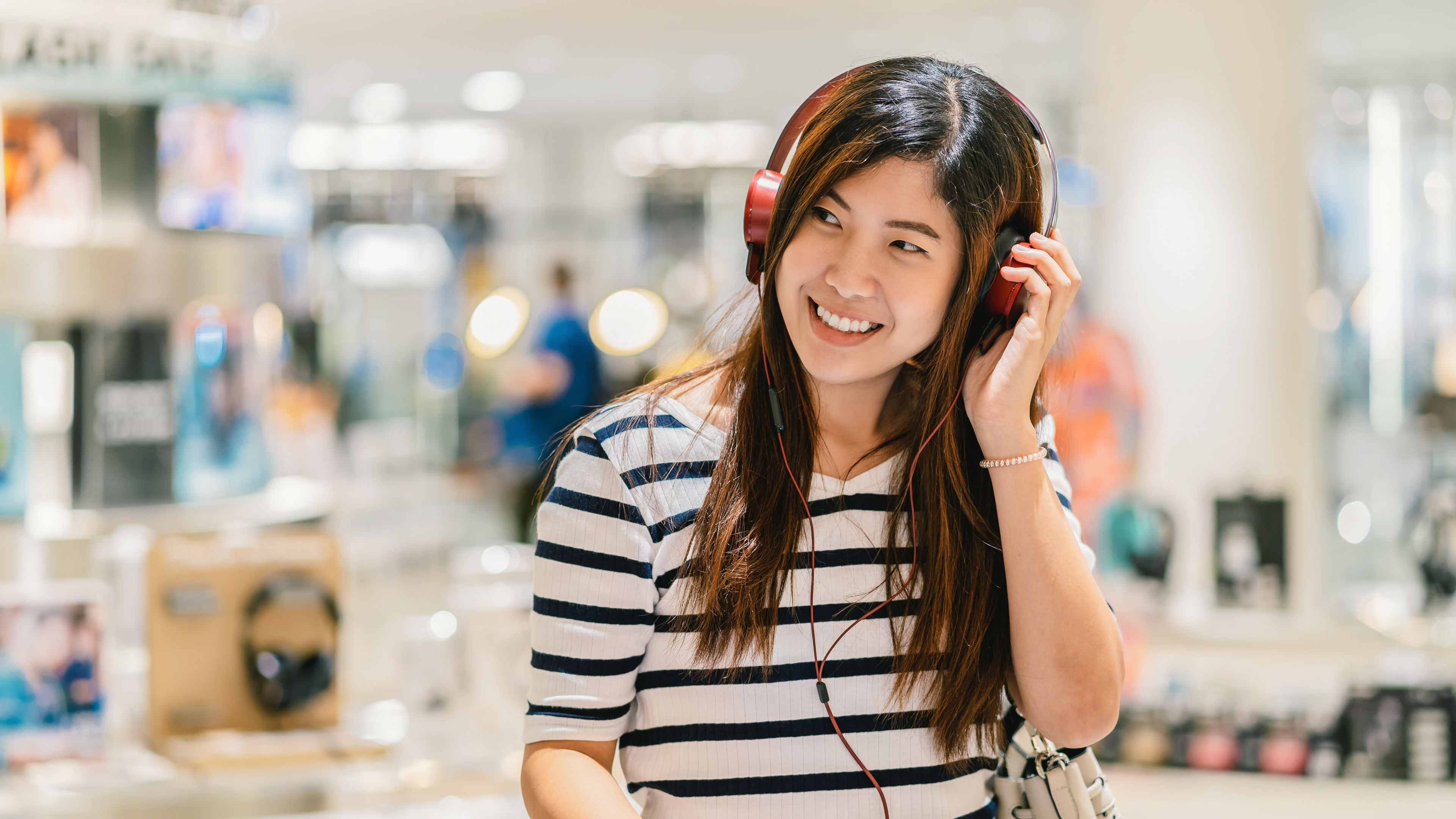 A happy woman testing headphones in an electronics store.