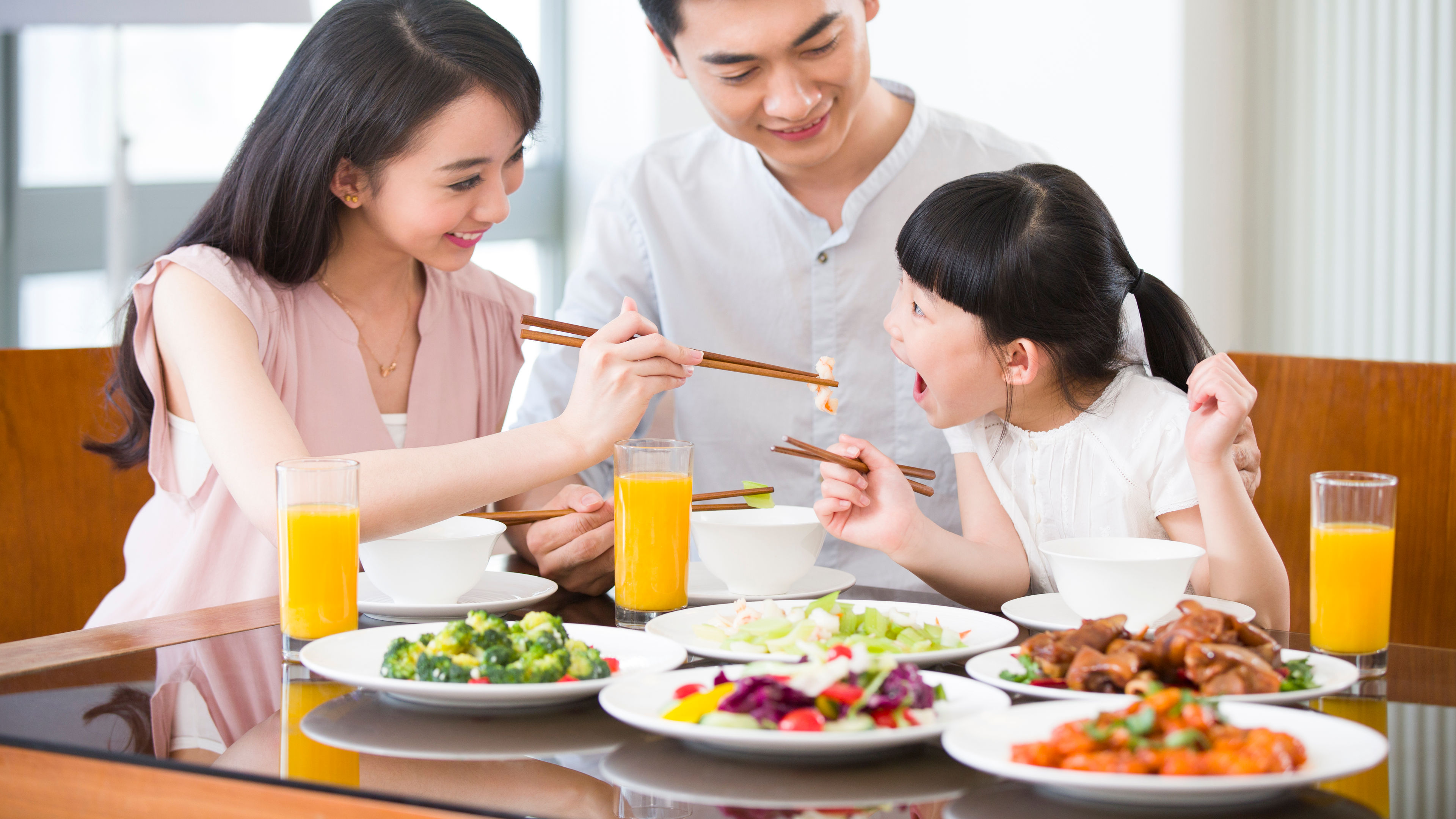 A happy family sits around a dining table, feeding each other and enjoying 