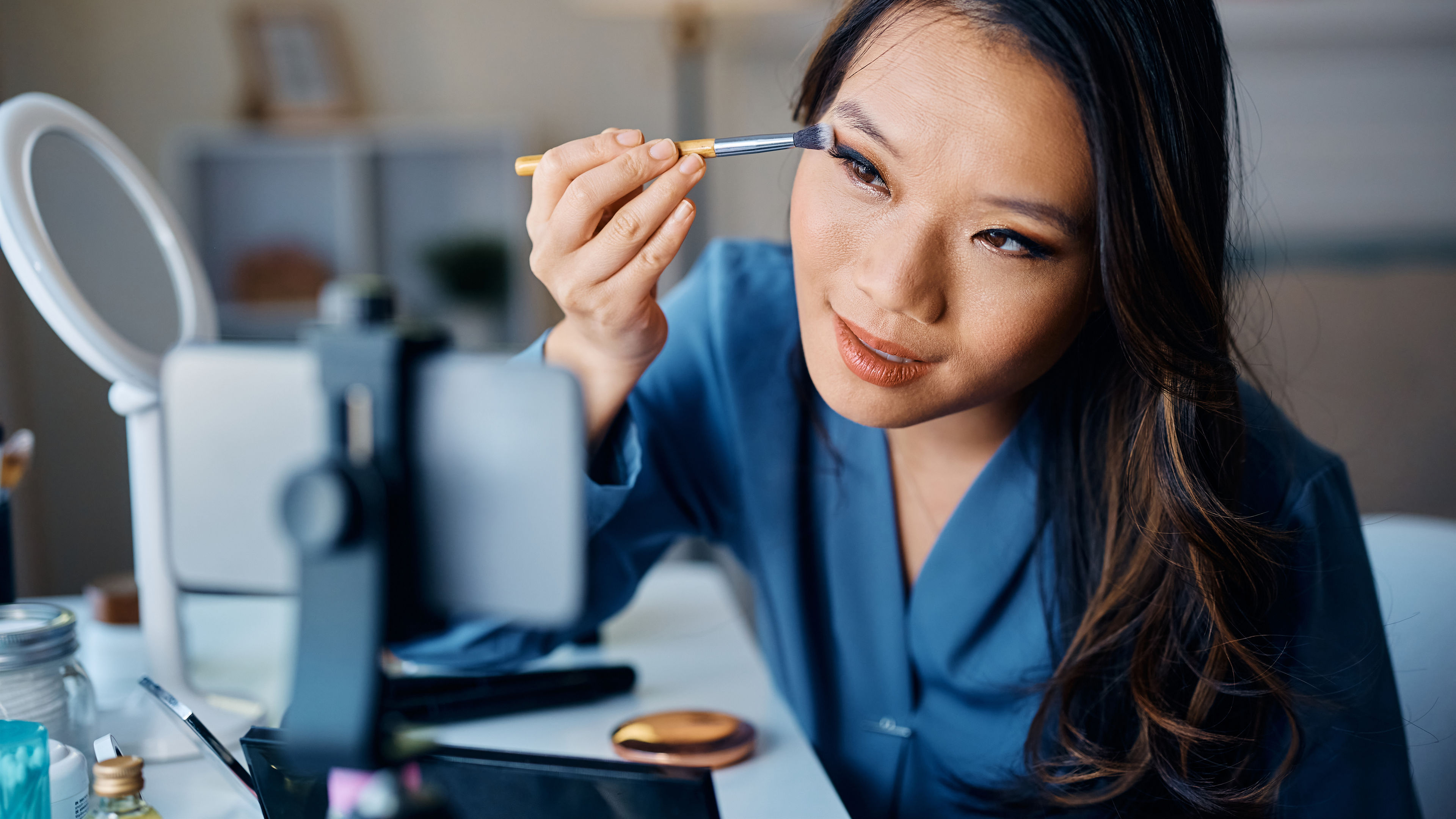 Young Asian woman applying eyeshadow wearing blue 