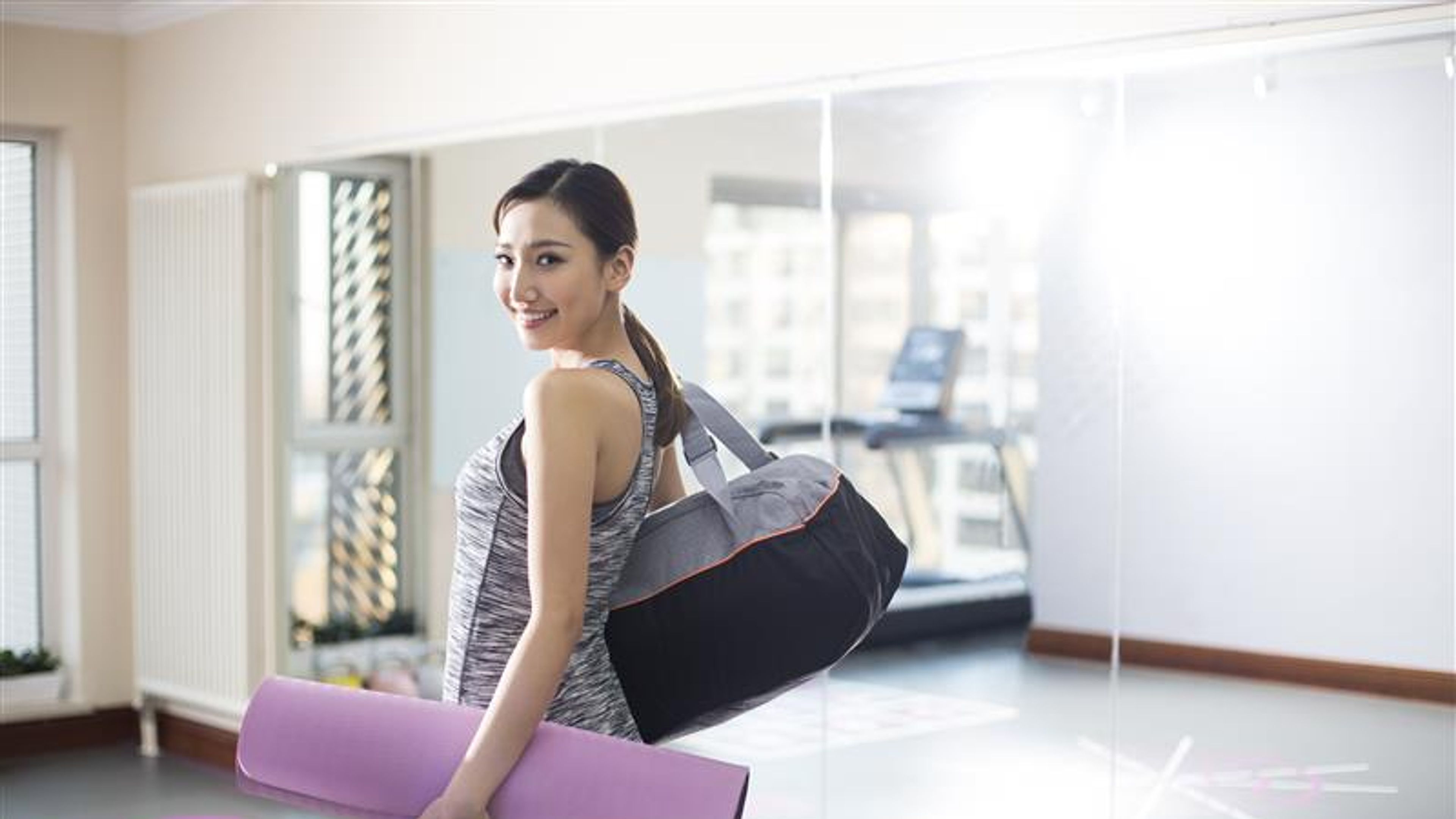 Young Chinese woman with yoga mat at gym 