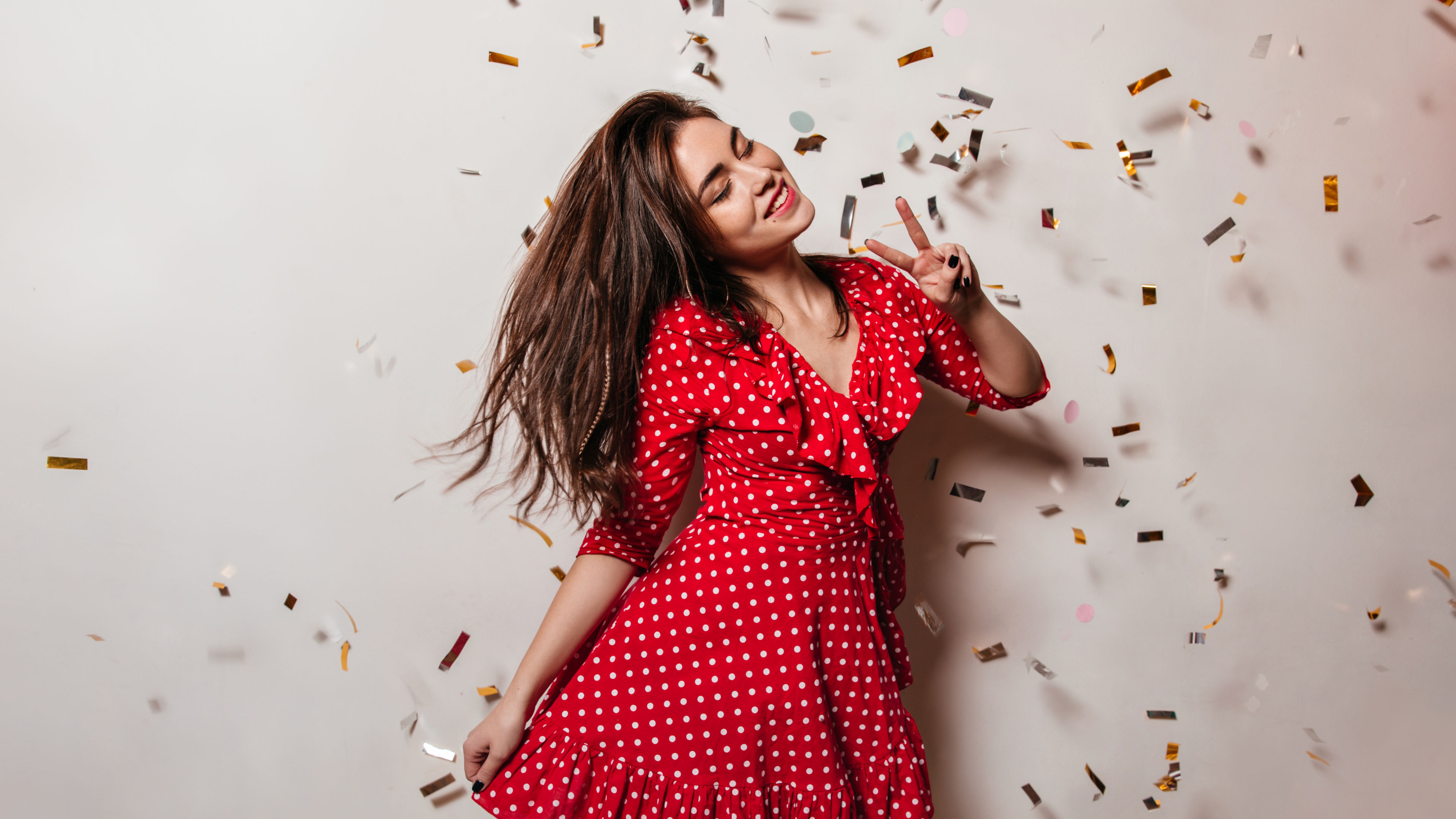 Young woman in high spirits is wearing red polka-dot dress. Girl with smile poses on background  