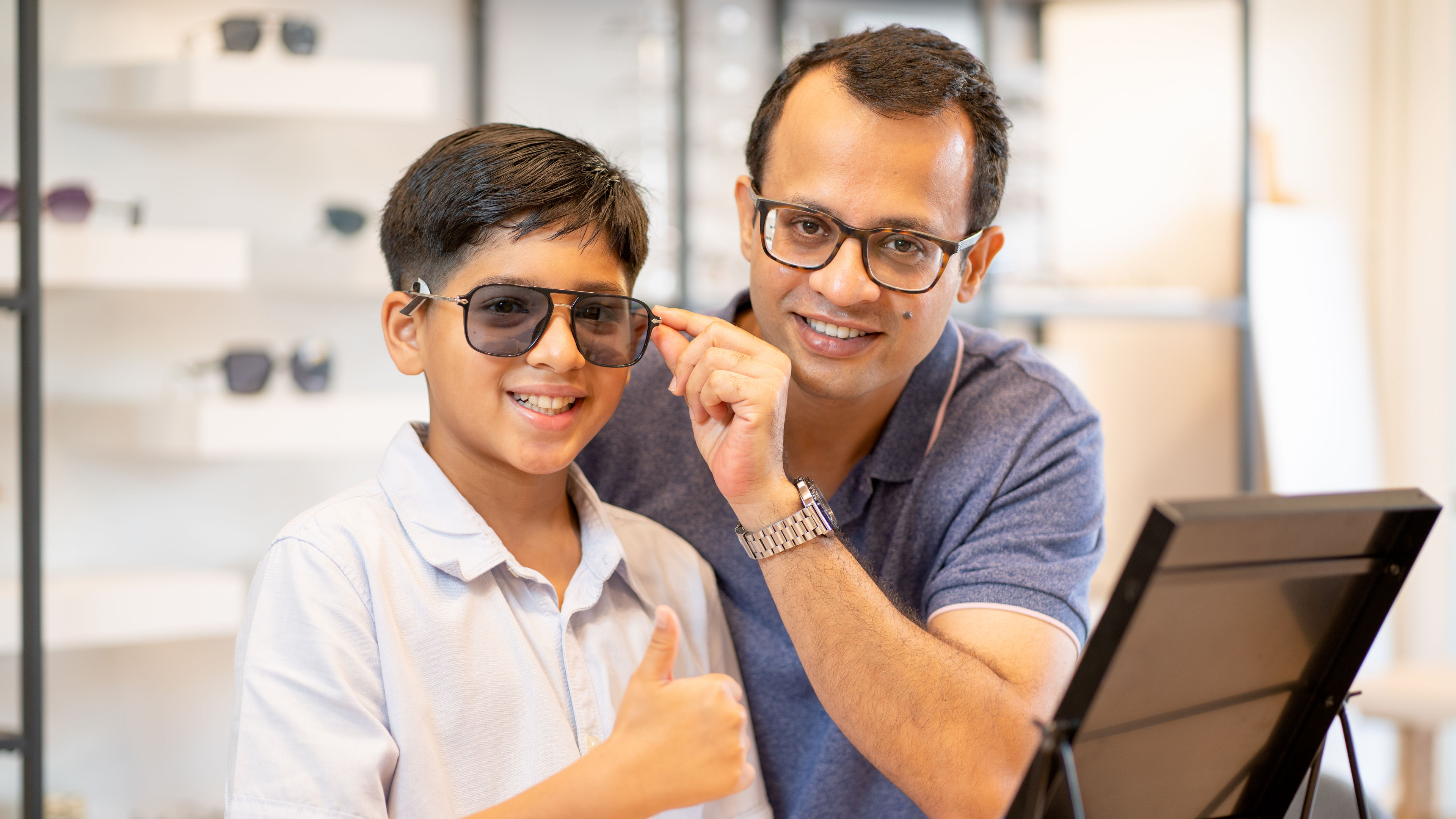 A Indian father and son checking out sunglasses in an eyewear shop.