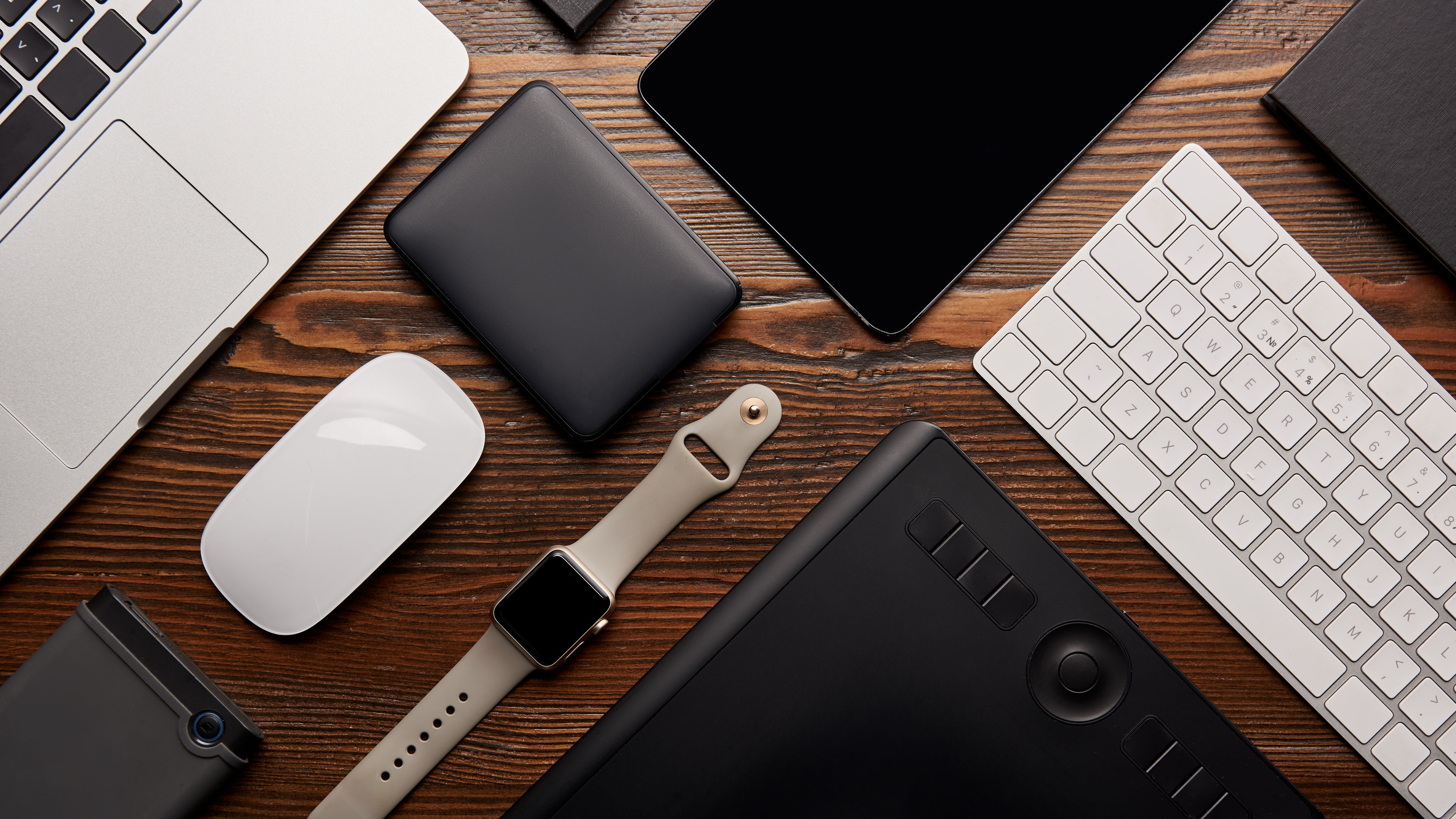 A flat lay showcases different electronic devices neatly arranged on a wooden workspace 
