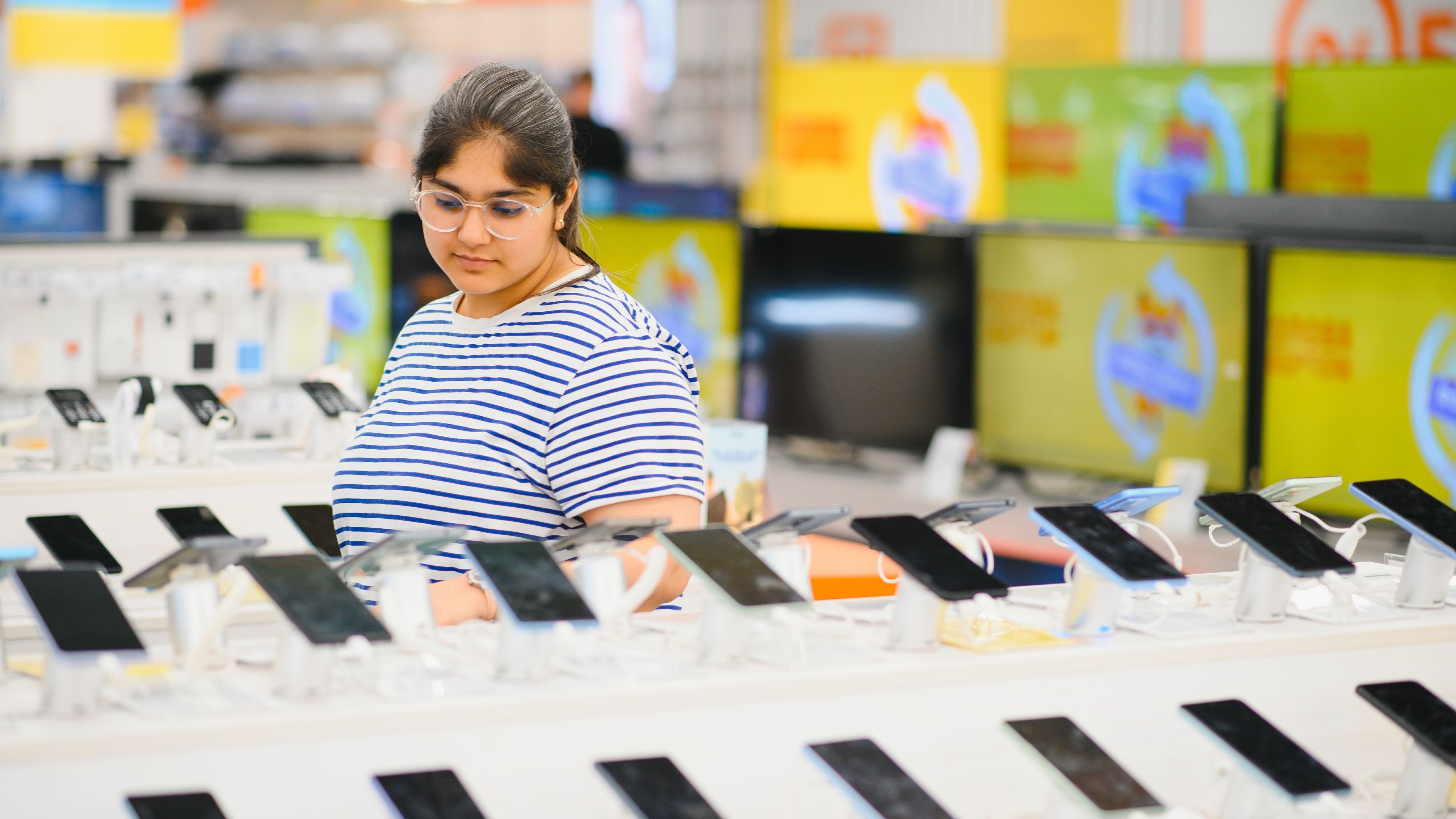 A young woman choosing smartphones in a shop 
