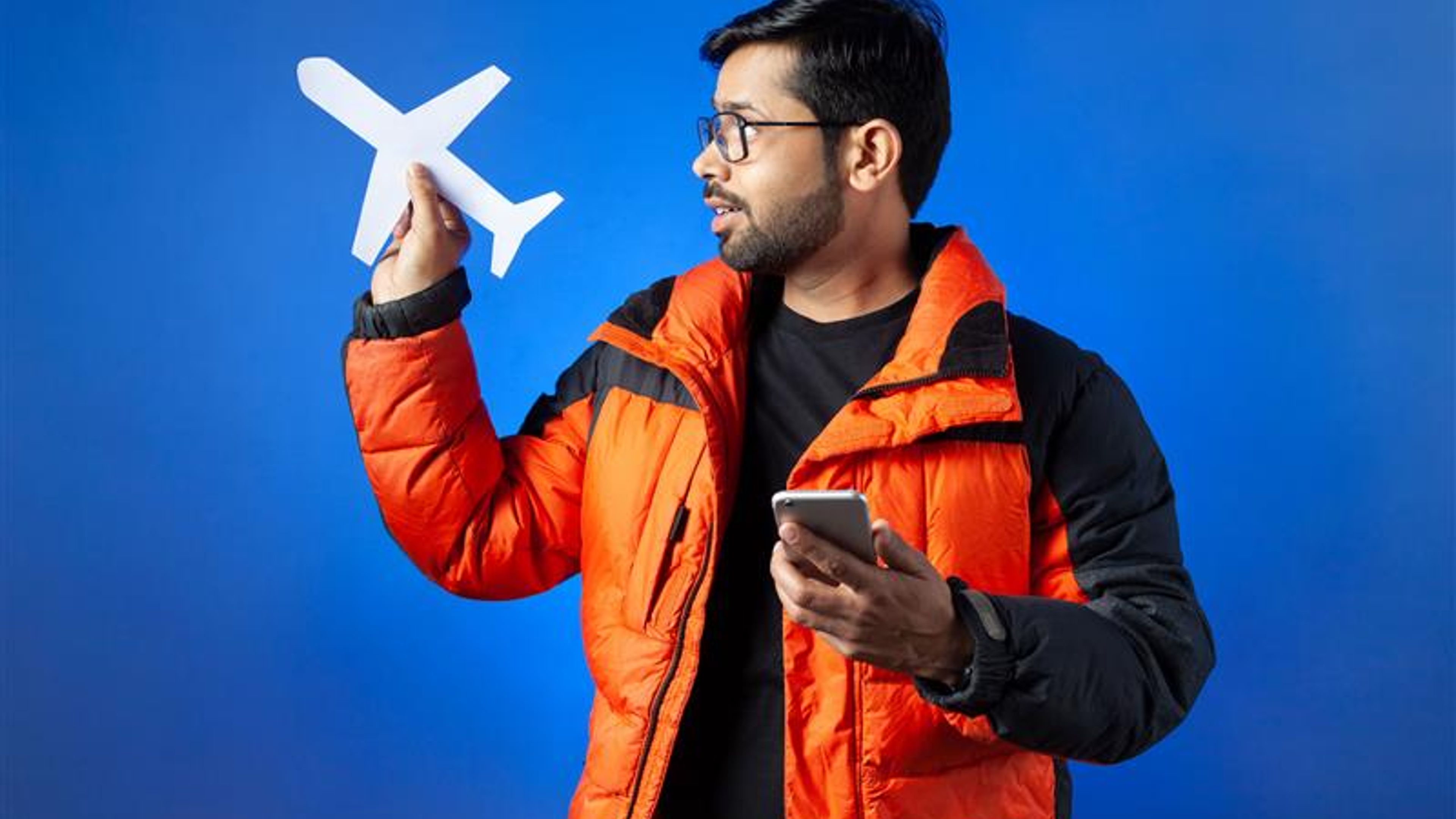 A young man clutching paper cut airplane and mobile phone. 