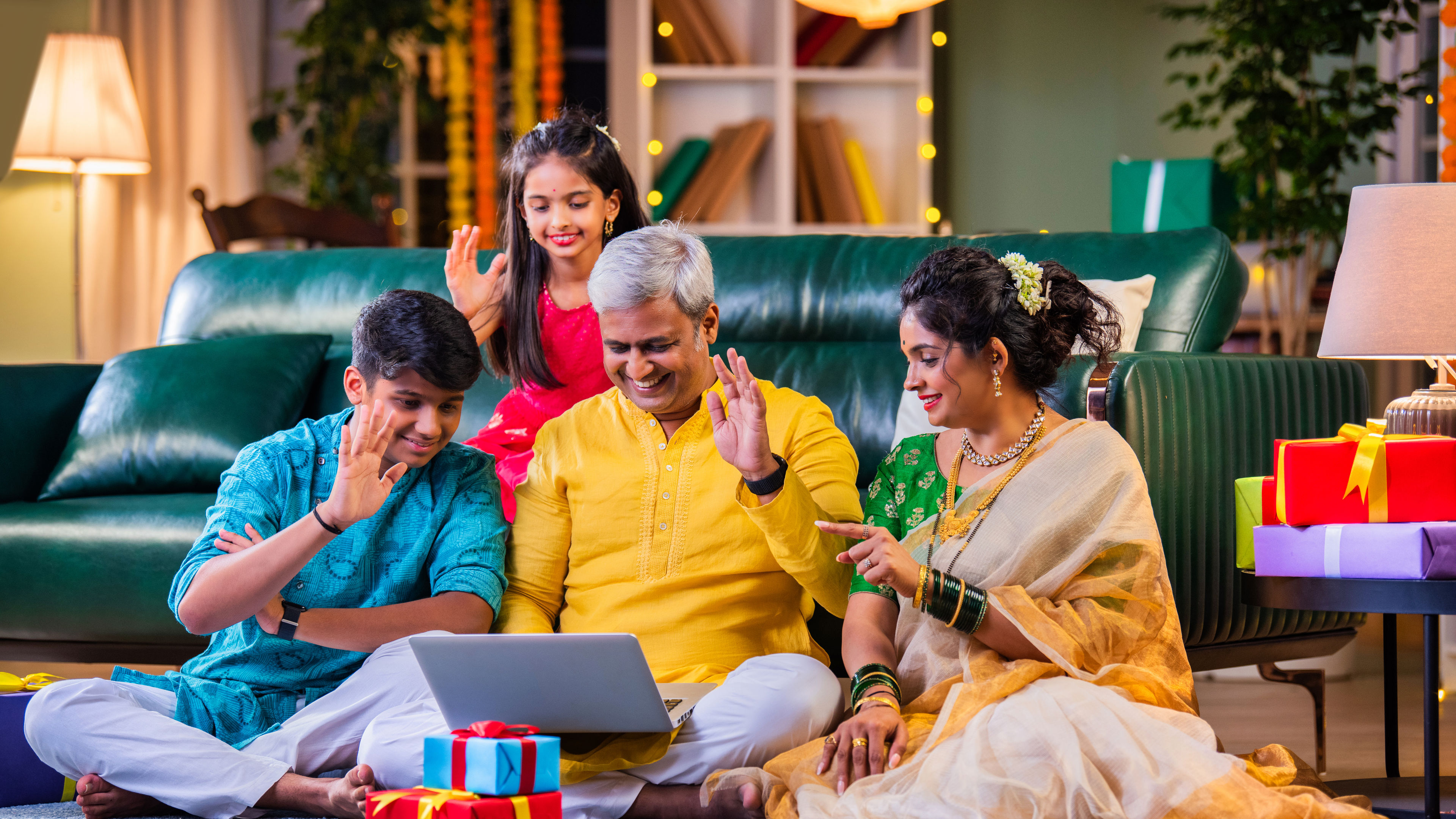 Indian family in festive attire making a video call during Diwali, surrounded by gifts on the sofa 