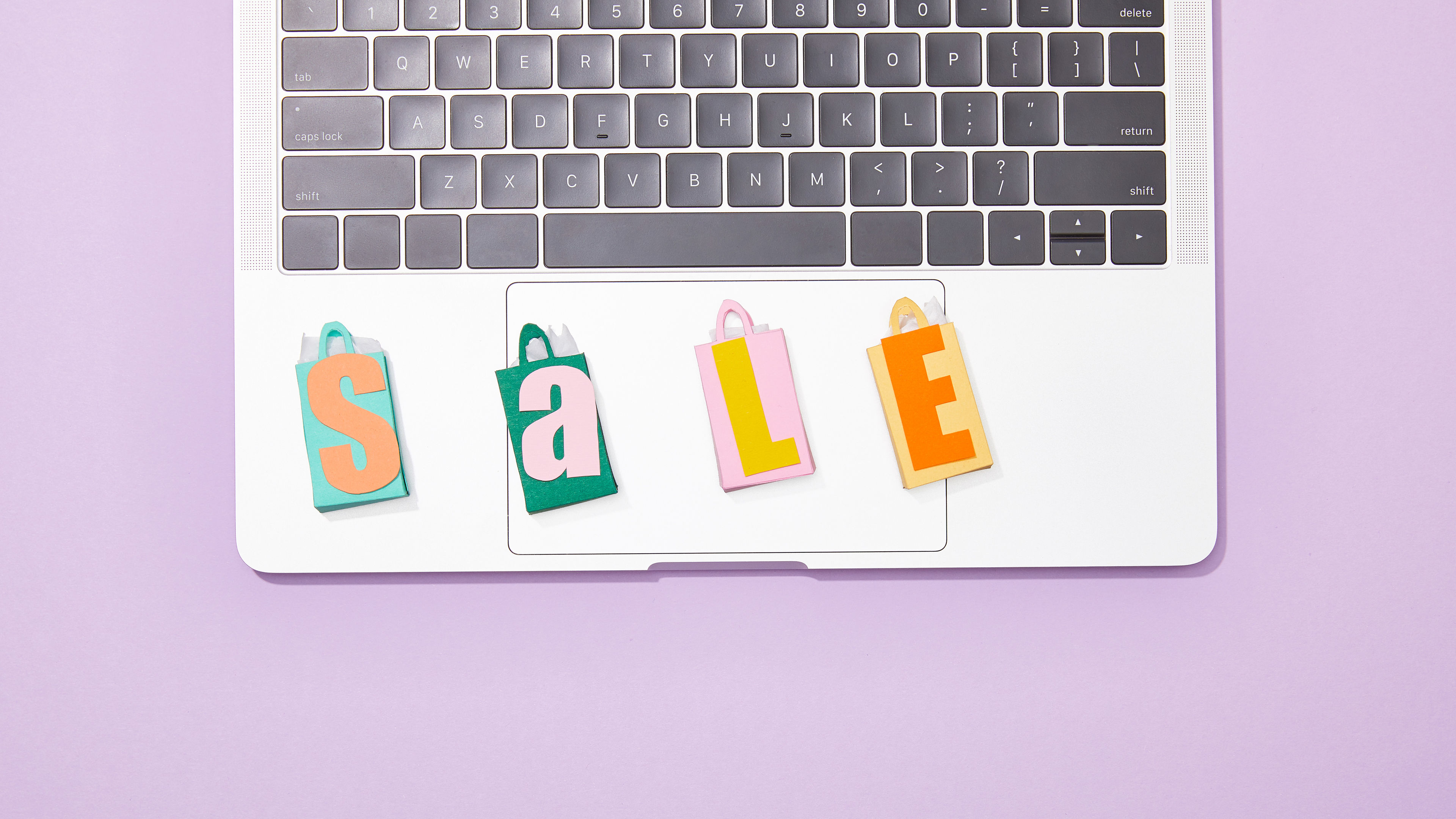 Colourful toy shopping bags with letters spelling "SALE" are neatly arranged on the keyboard of a laptop 