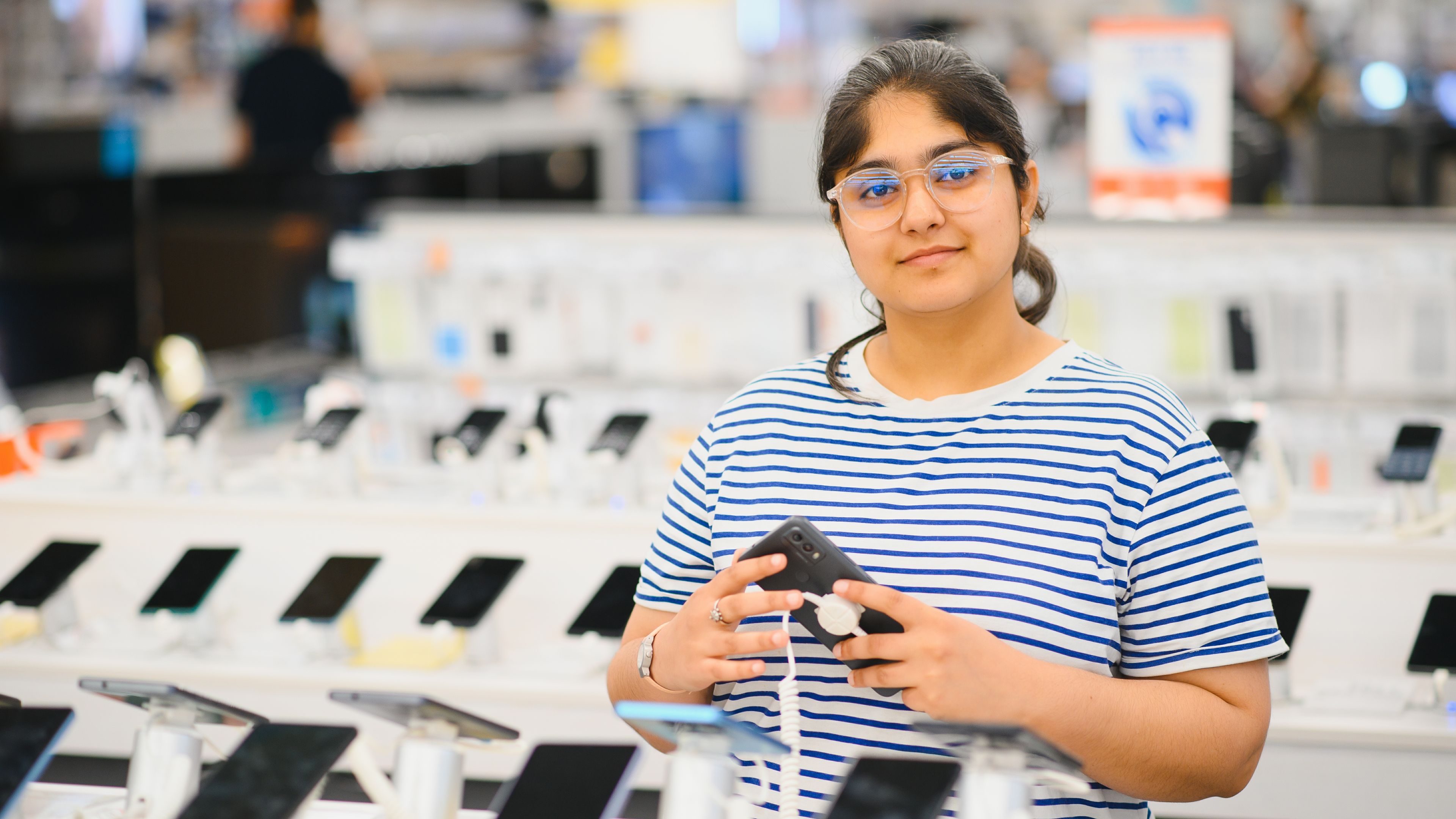 Woman examines options while choosing a new mobile phone in a brightly lit shop 