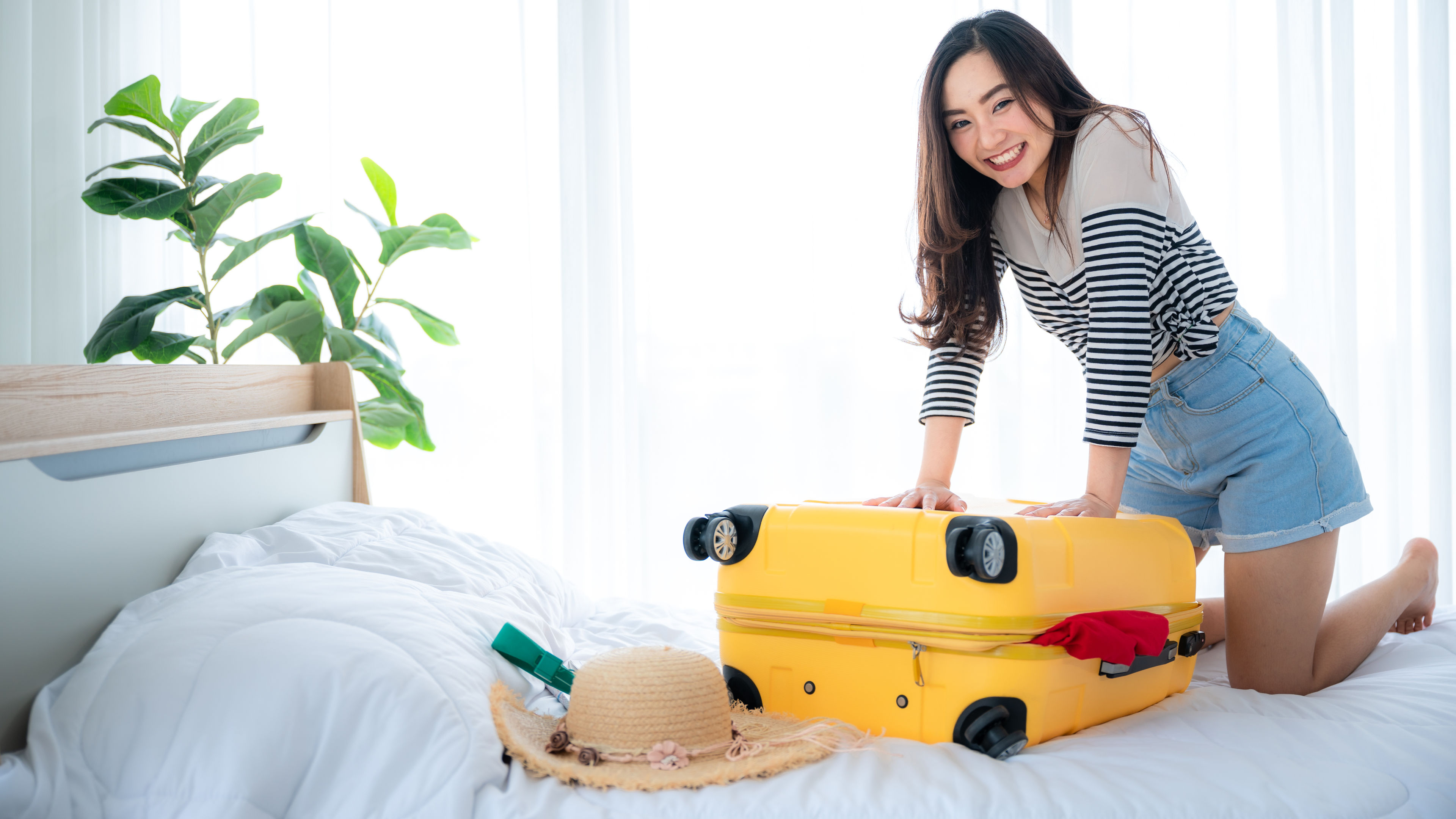 A cheerful Asian woman traveler with packed yellow suitcase.