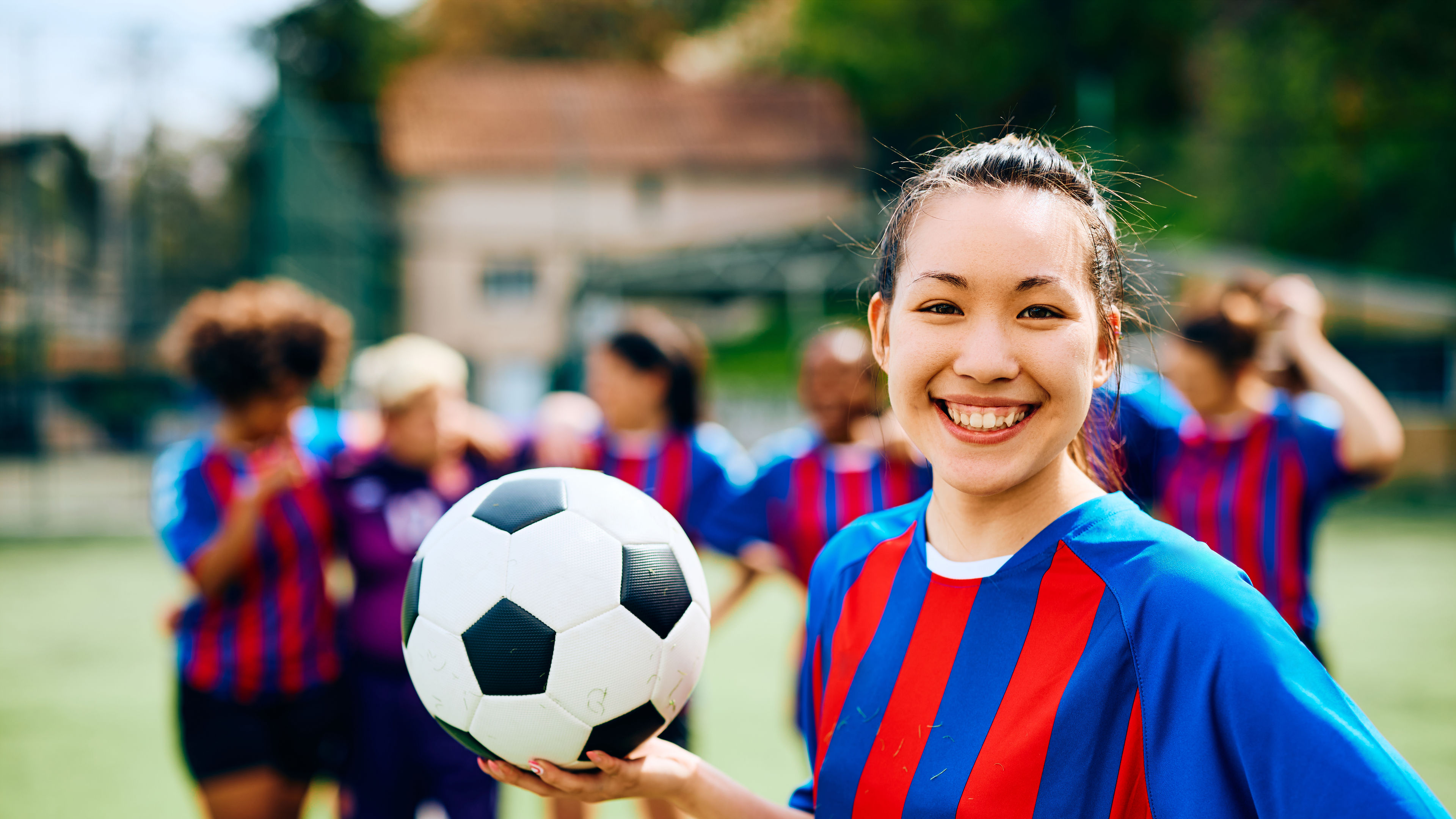 A happy female soccer player posing with football in hand.