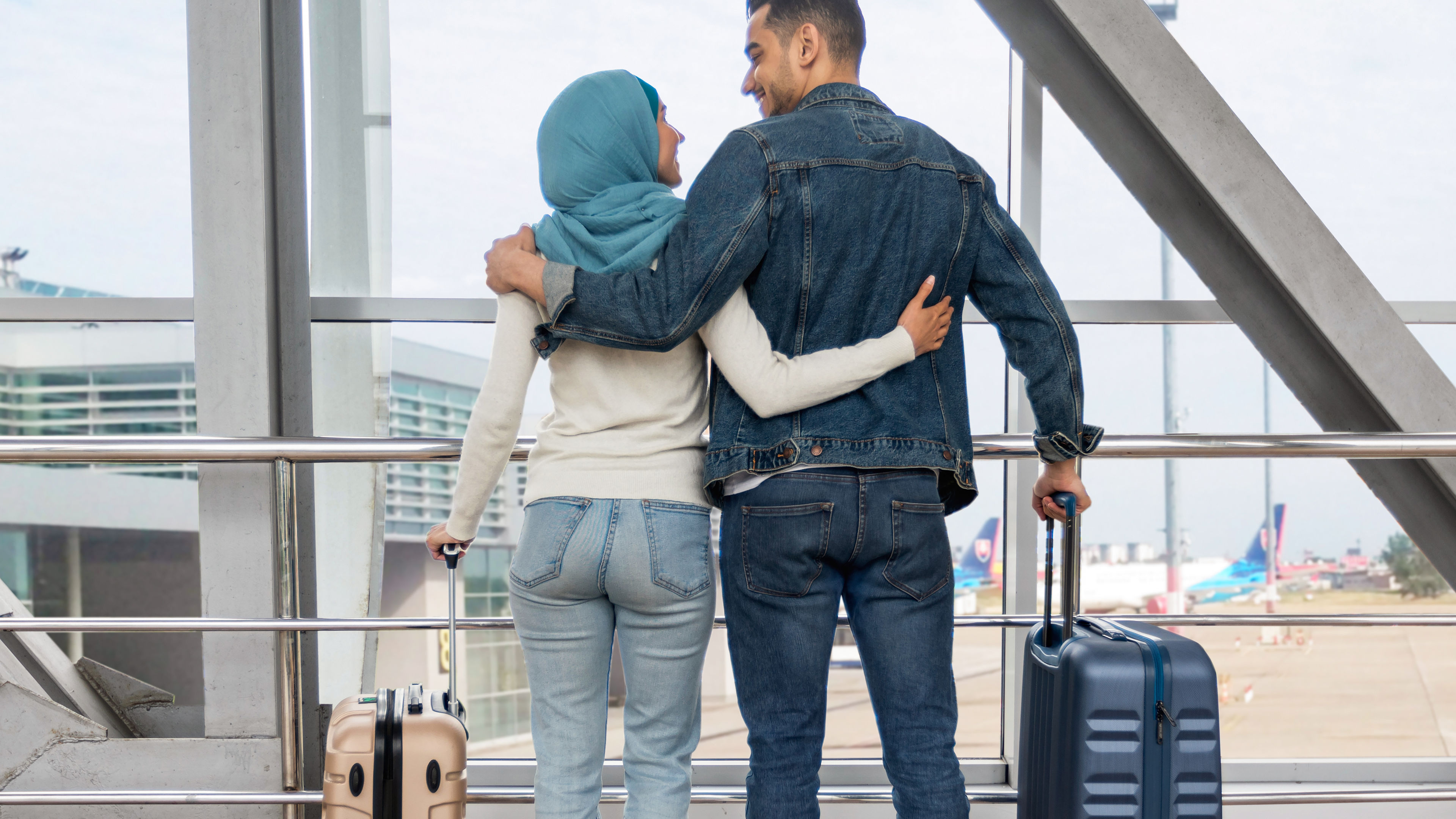 Romantic Travel. Loving Muslim Couple Standing With Suitcases Near Window In Airport