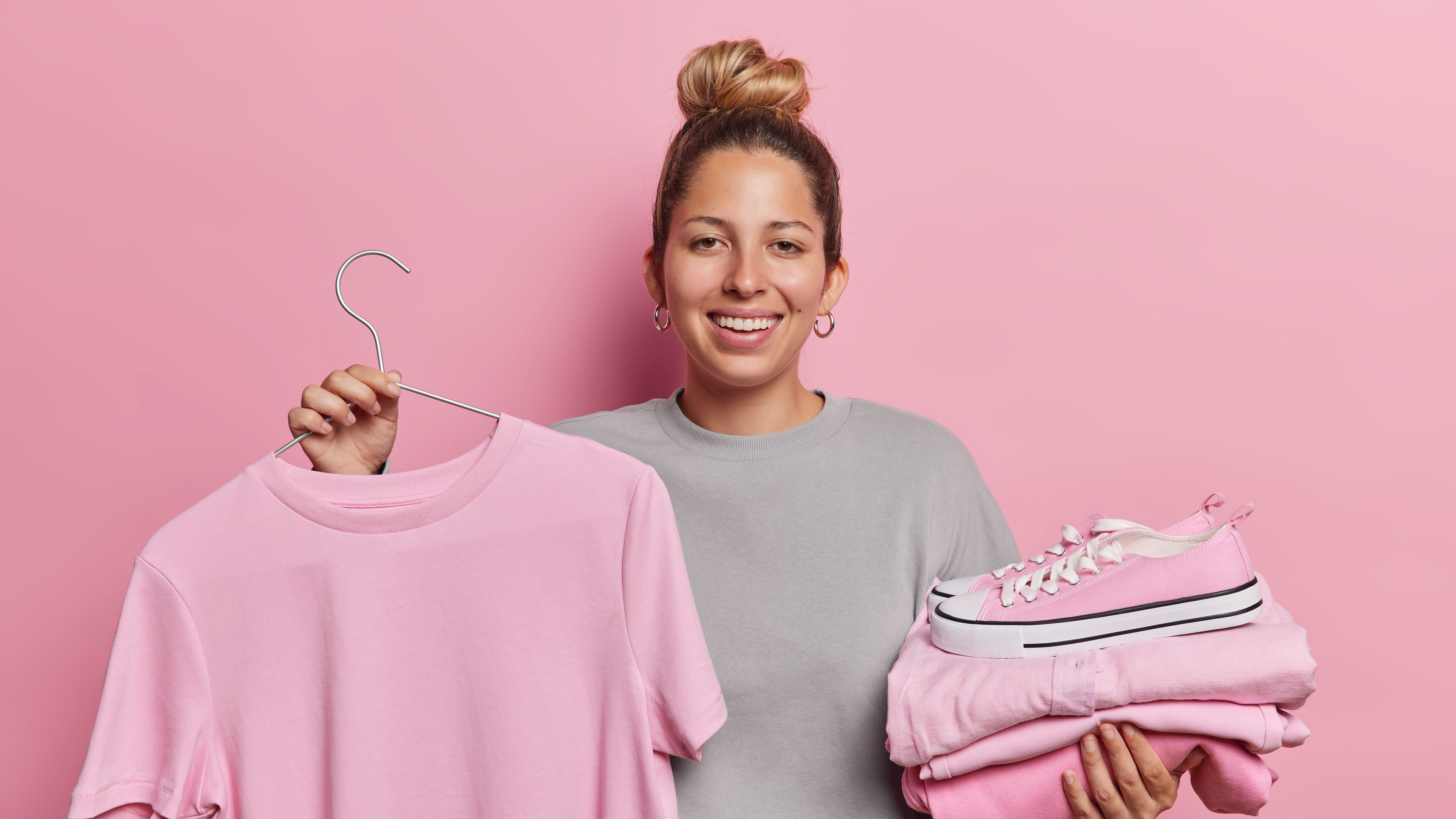 A smiling woman is holding a pink t-shirt on a hanger