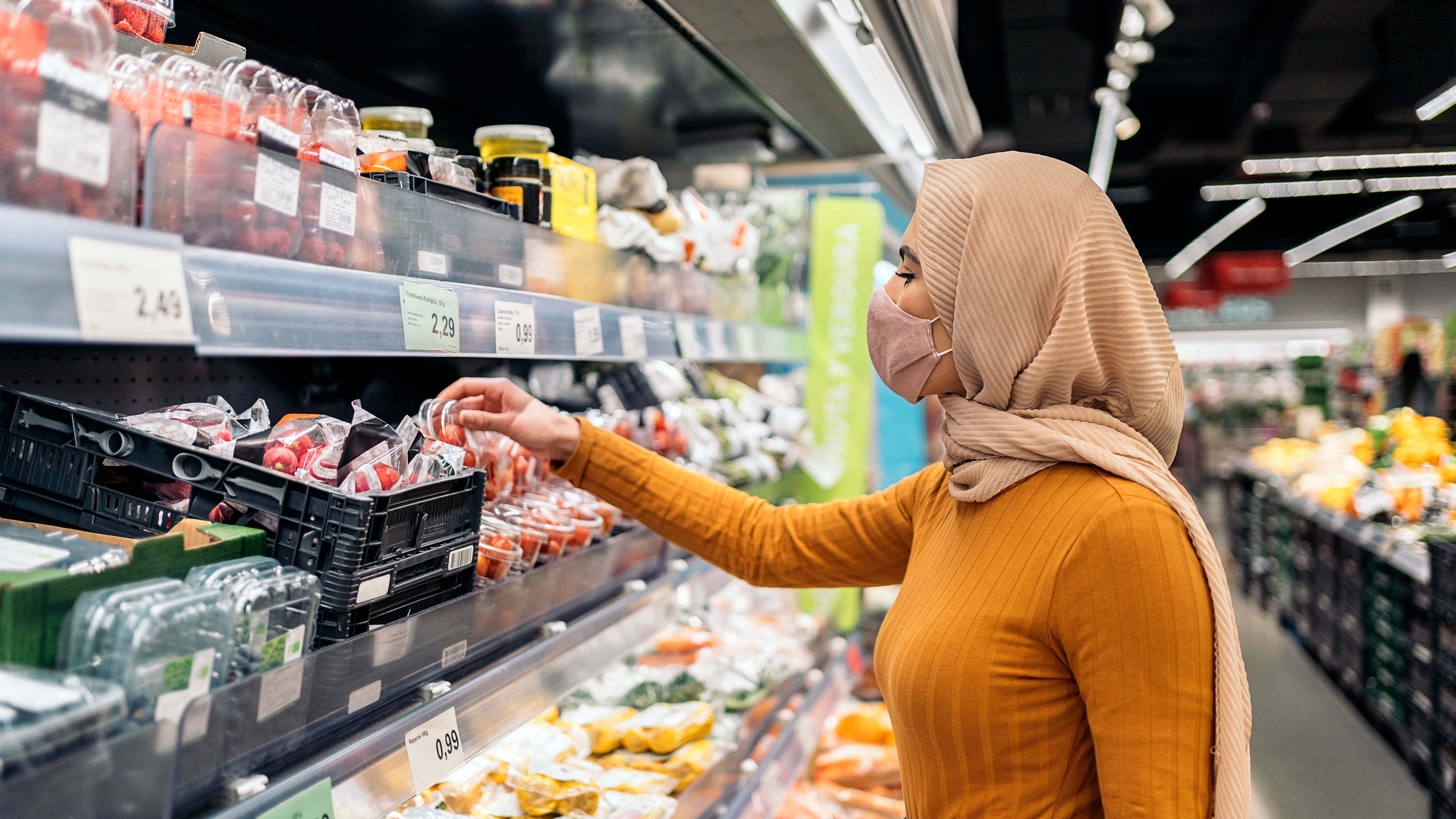 Seorang wanita muda memakai tudung, memegang beg membeli-belah, dan berjalan di jalan membeli-belah sambil membuat panggilan telefon. 