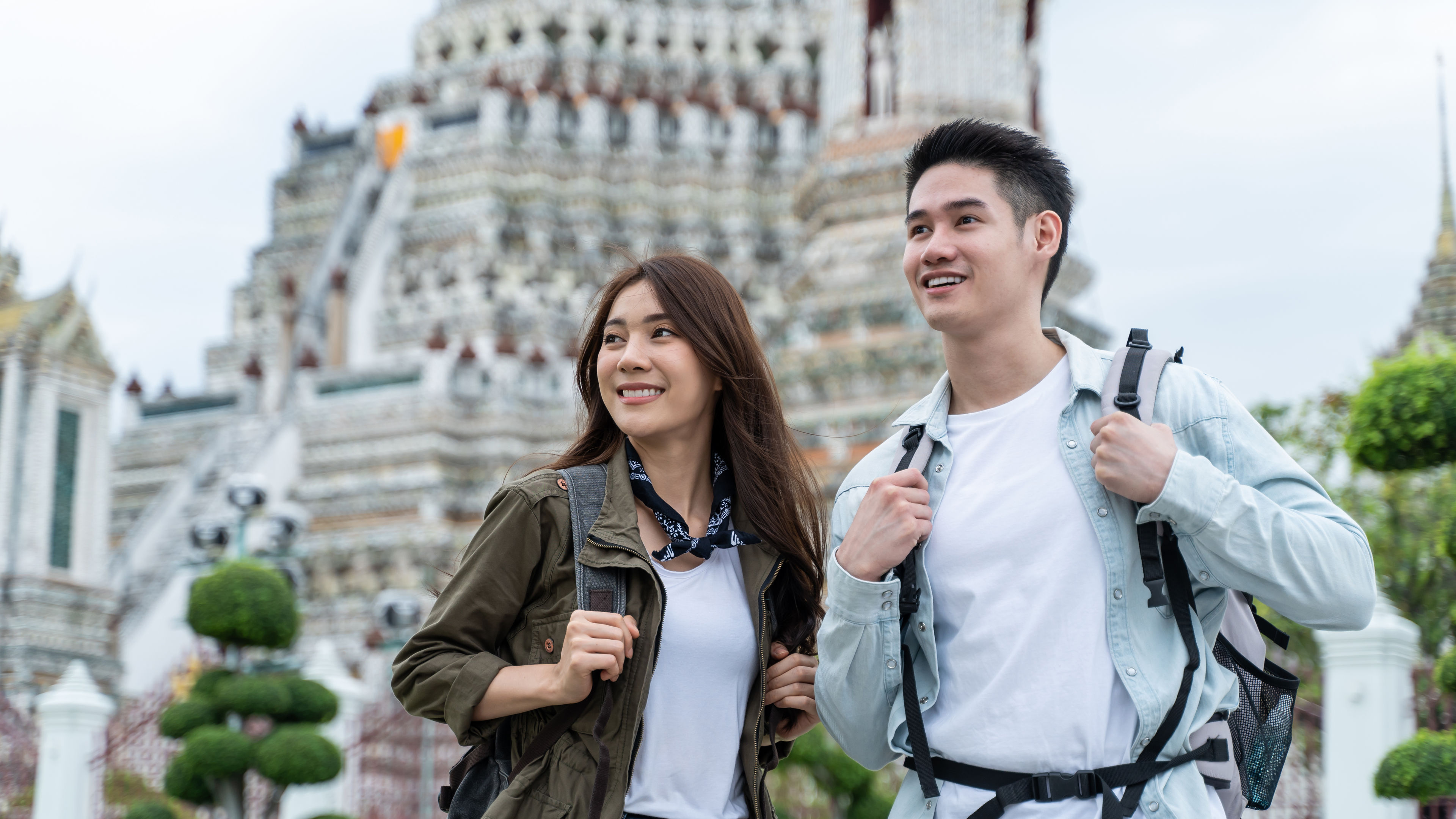 A young Asian couple stands together with backpacks.