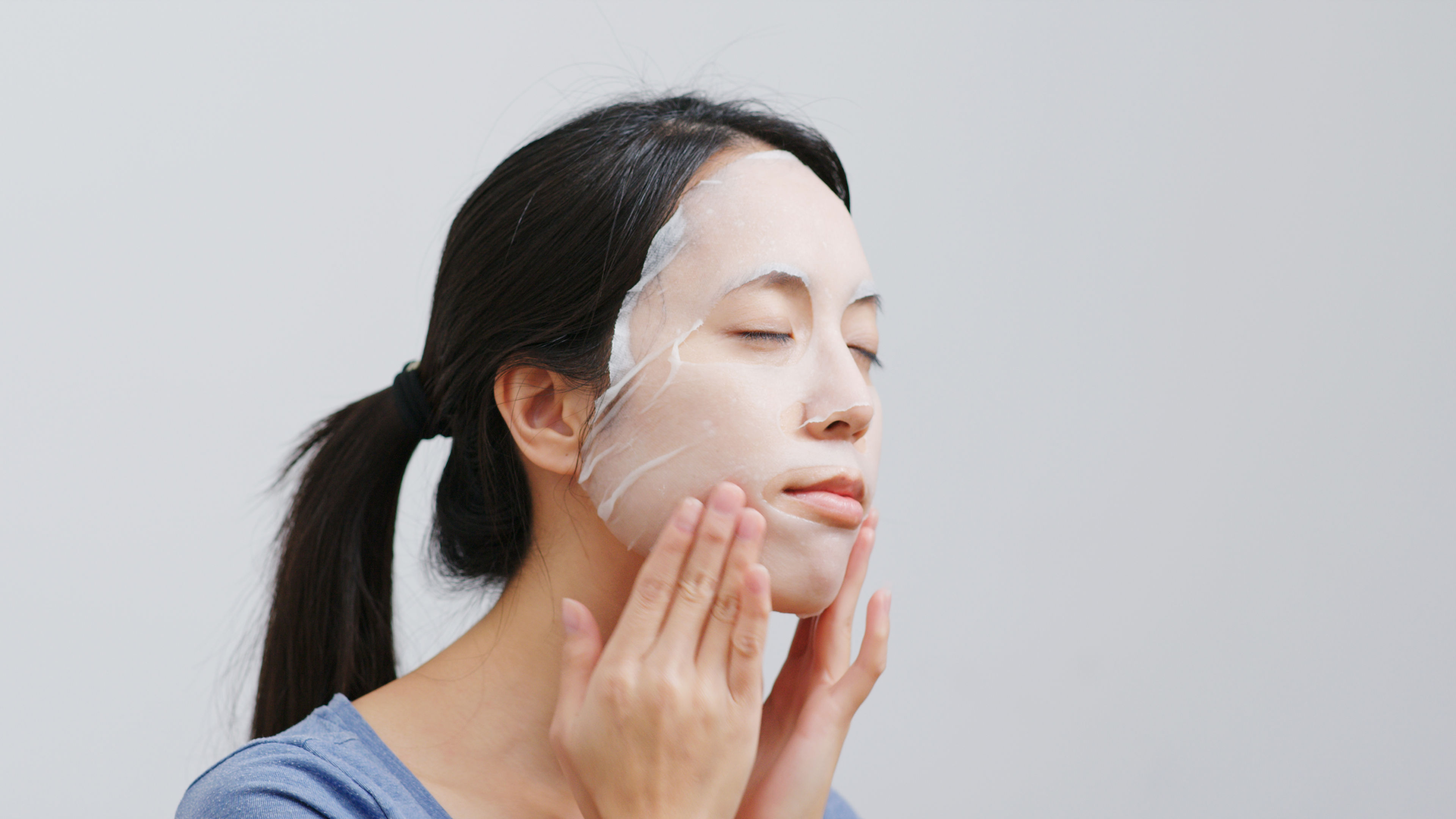 A young woman sits comfortably in her home, gently applying a rejuvenating face mask 