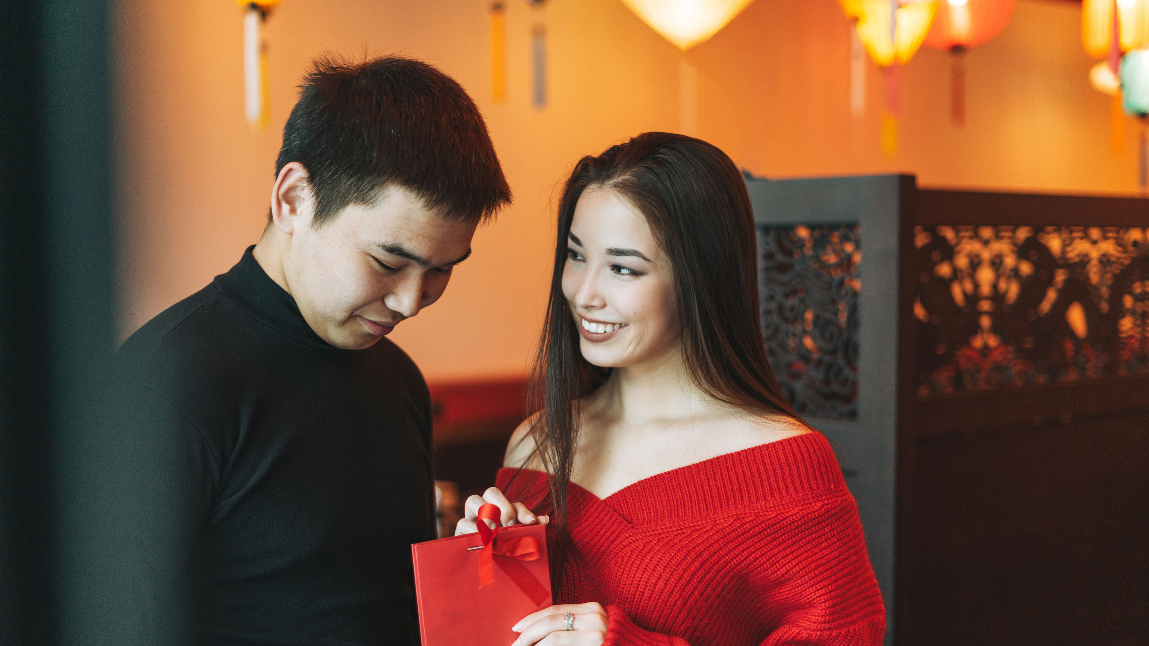 Beautiful young asian couple in red clothes give present in cafe 
