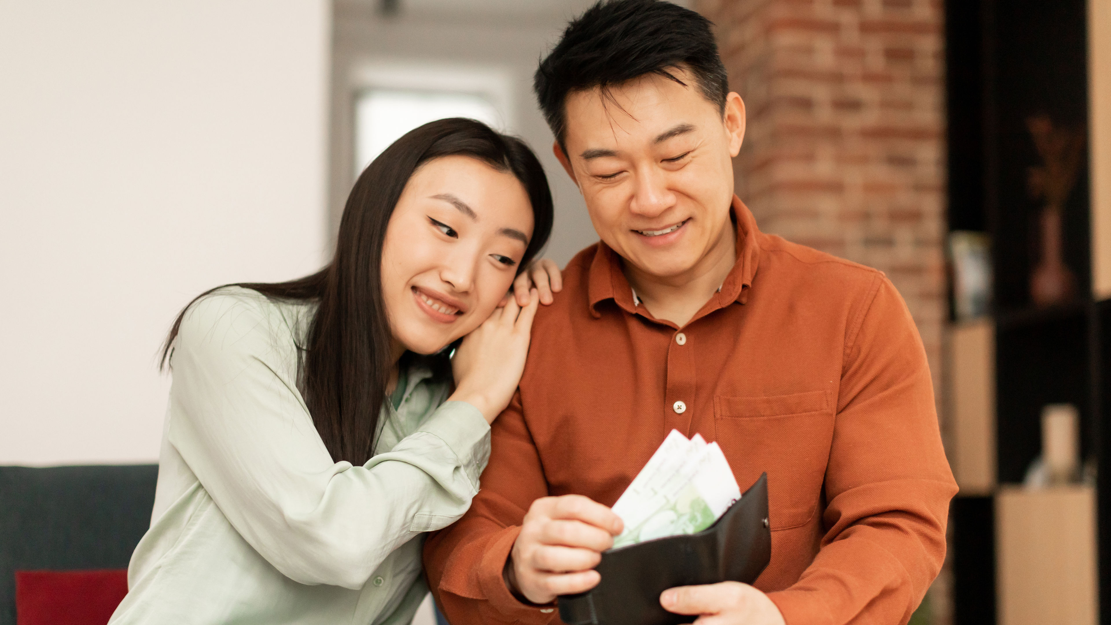 Finance and money saving concept. Happy asian man putting banknotes into wallet and smiling, sitting. 