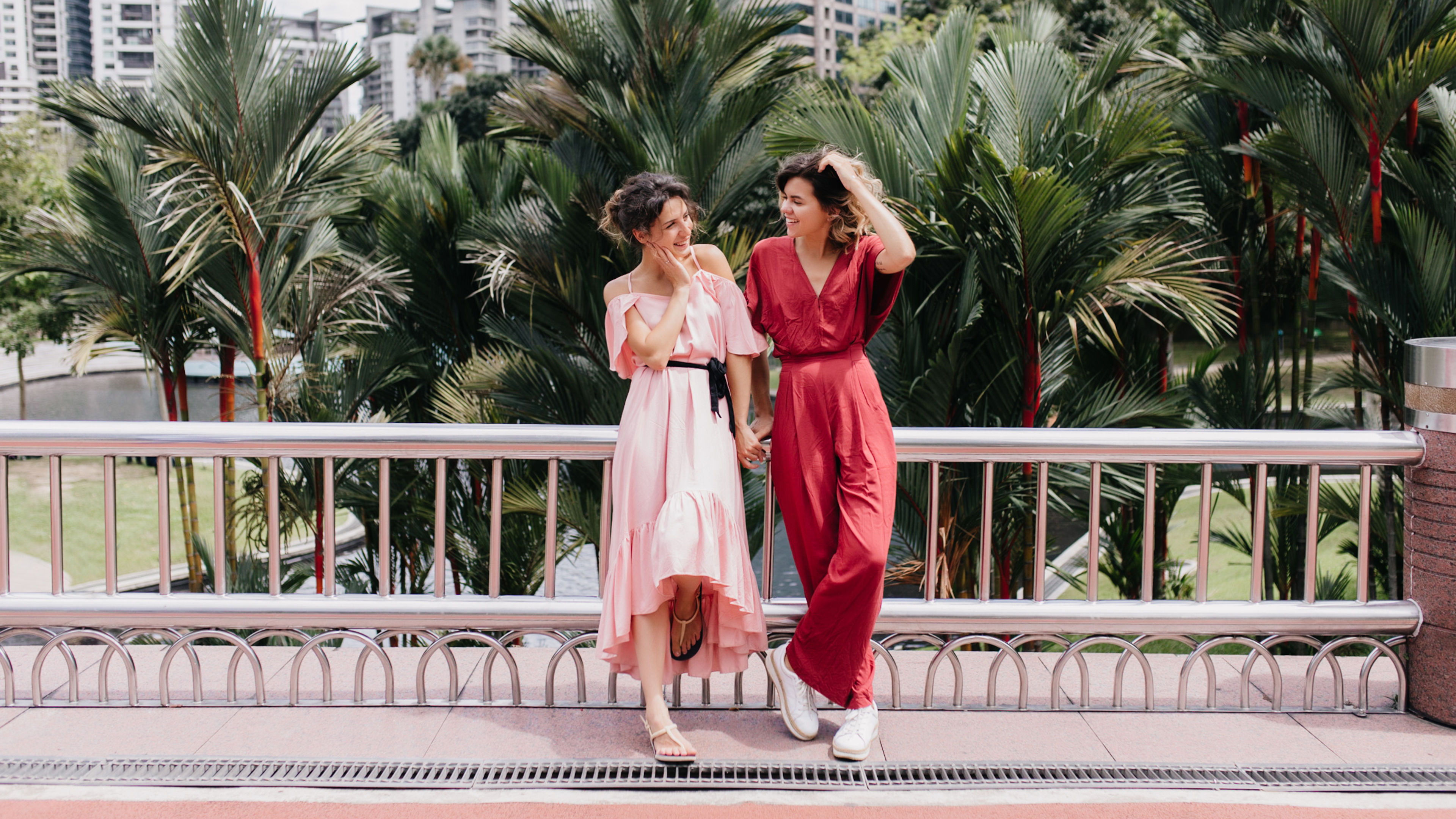 Full-length portrait of elegant girl in red attire touching her hair. Pretty ladies looking at each 