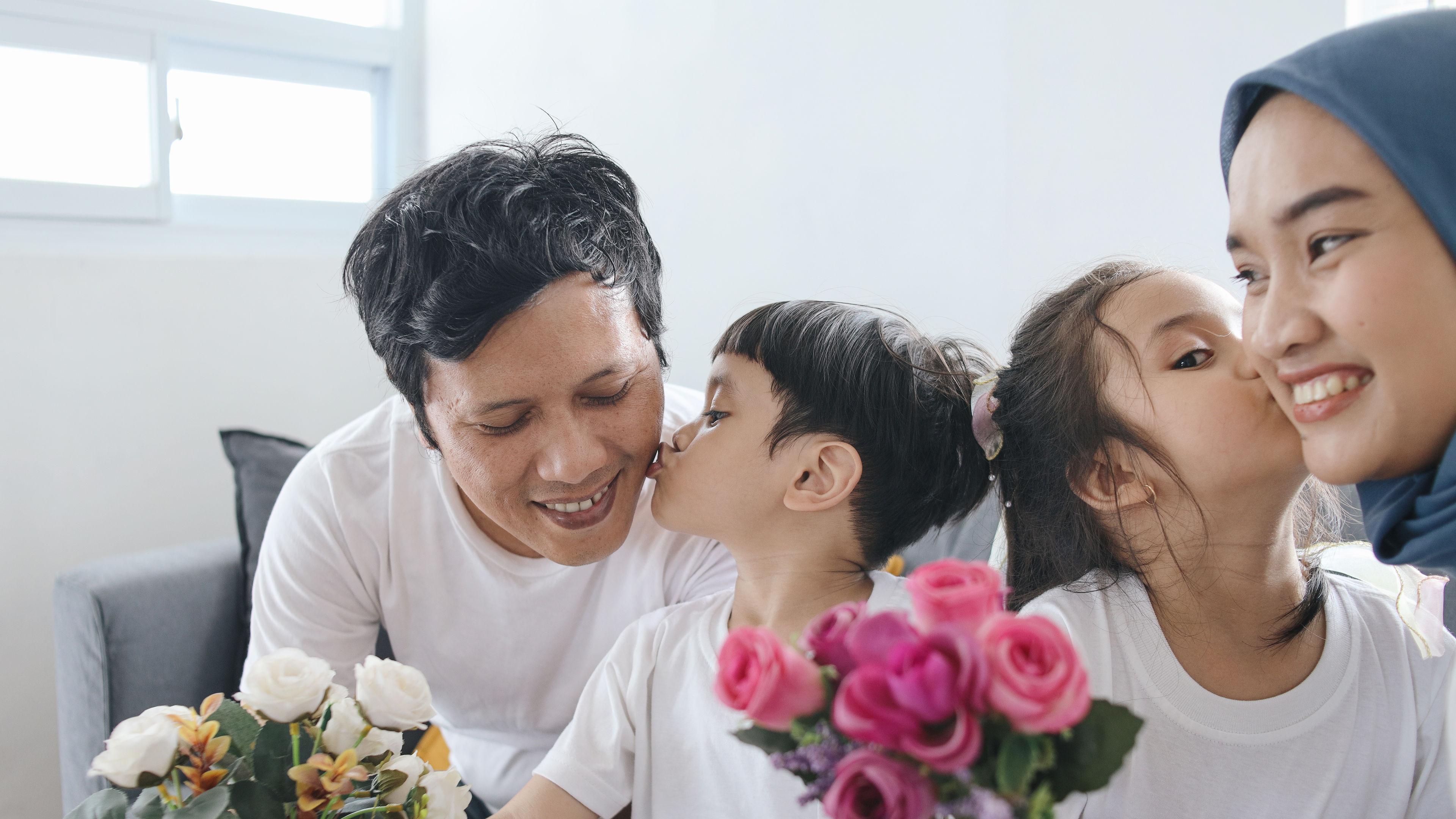 Kids Kissing Parents And Giving Flowers. Son Kiss Father and Daughter Kiss Mother at Home. Family Bonding. 