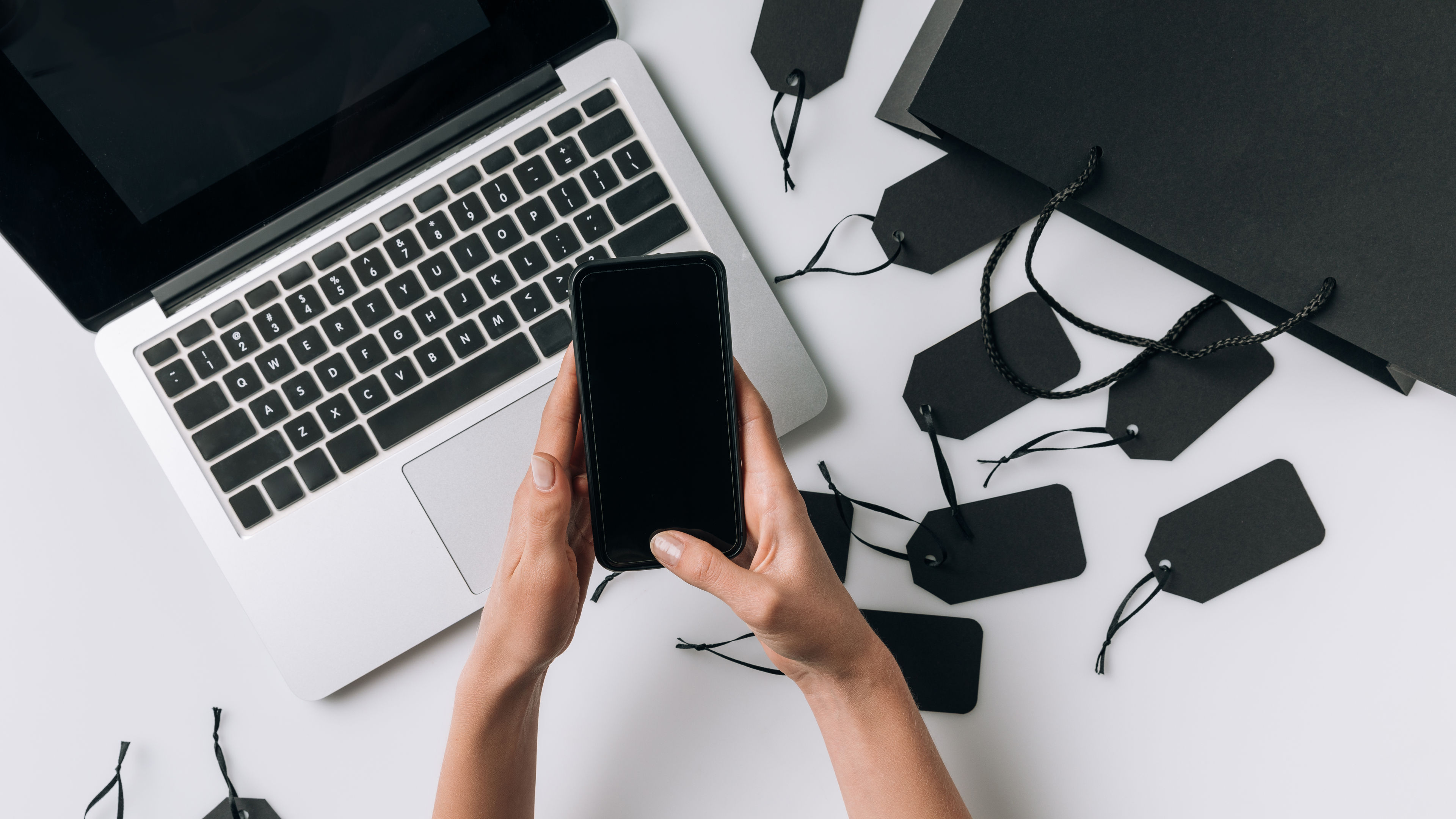 Partial view of female hands with smartphone, black blank labels and shopping bag isolated on white 