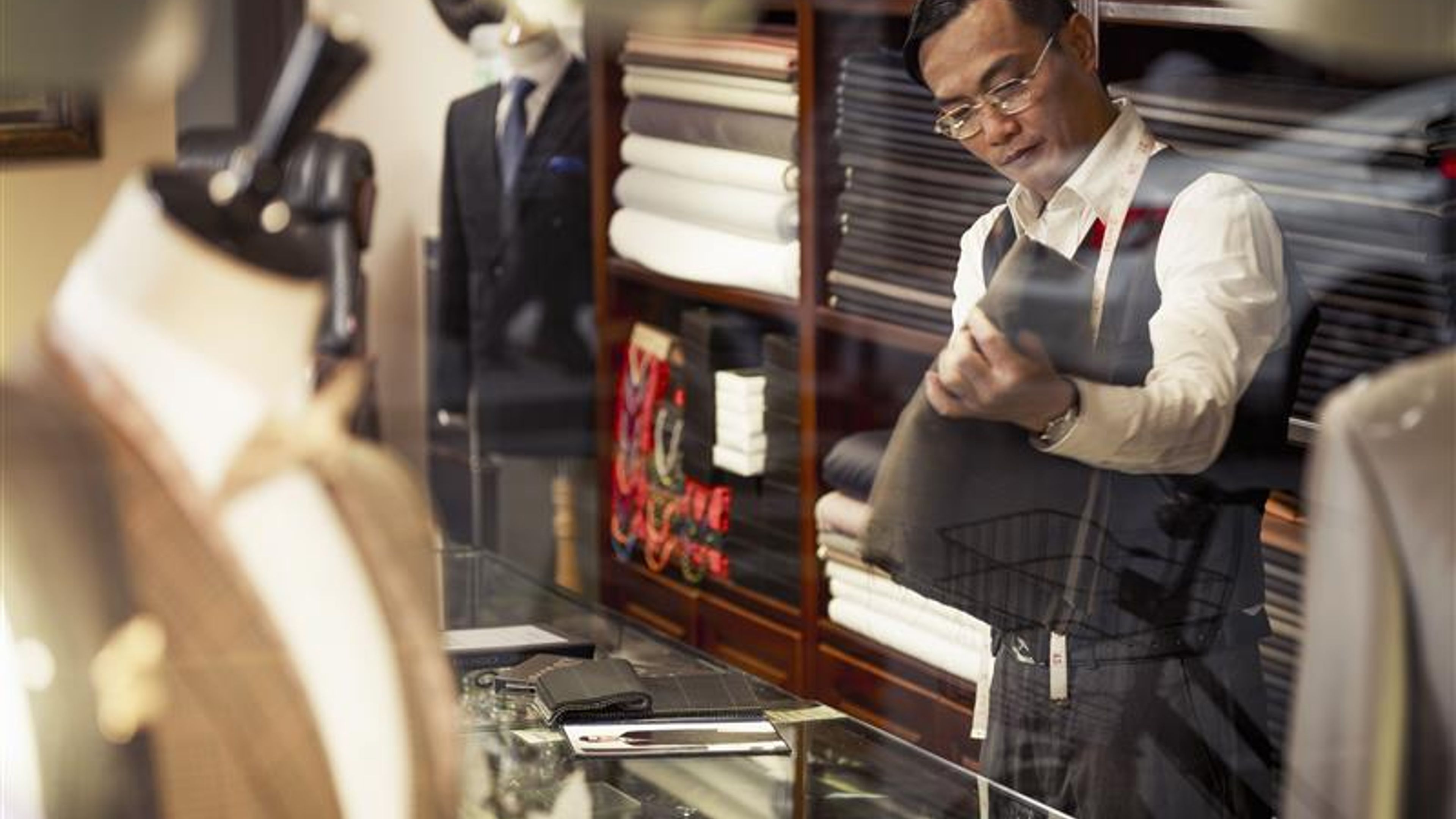 Tailor looking at fabric in traditional tailors shop 
