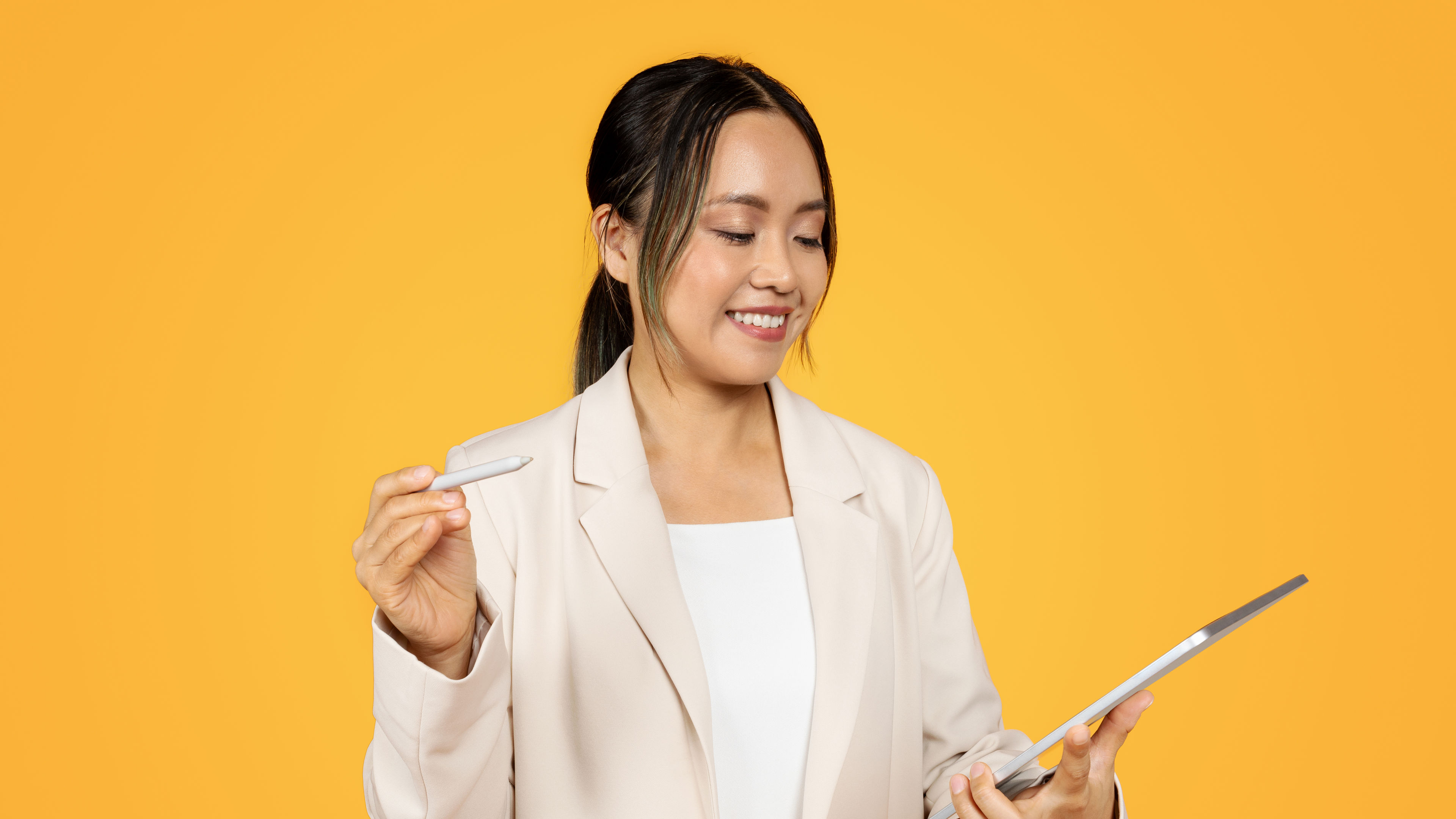 Woman holding tablet, yellow background. Woman smiling with stylus 