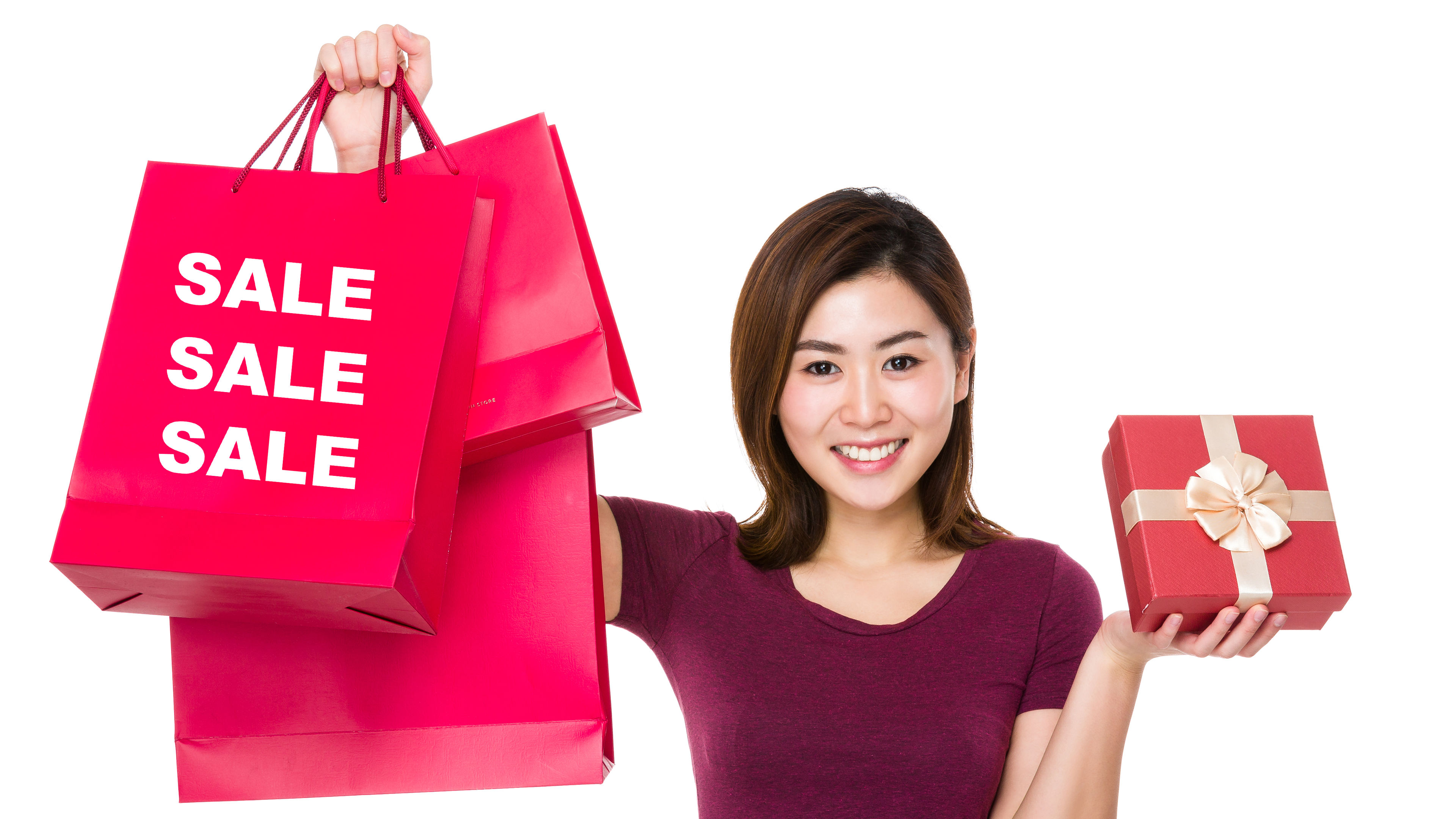 A smiling woman proudly holds shopping bags and a beautifully wrapped gift box, ready for festive surprises. 