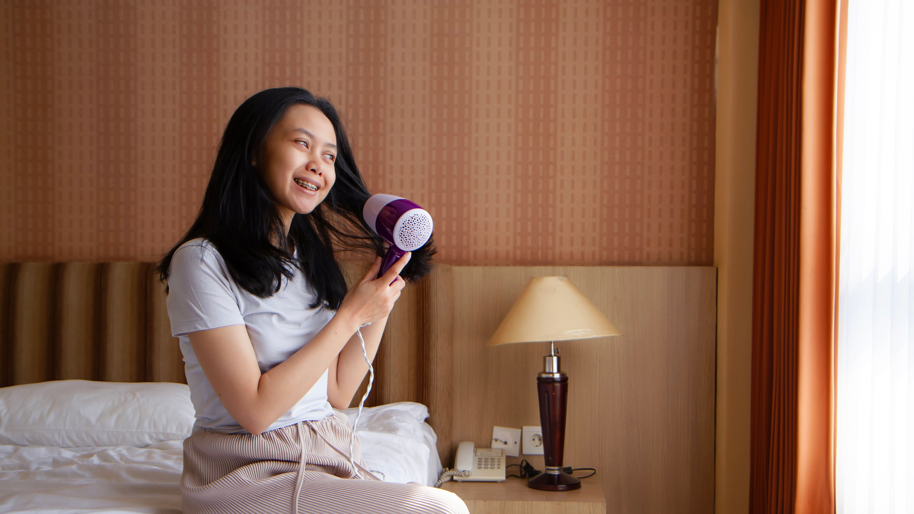 Woman sitting on bed blow drying hair 