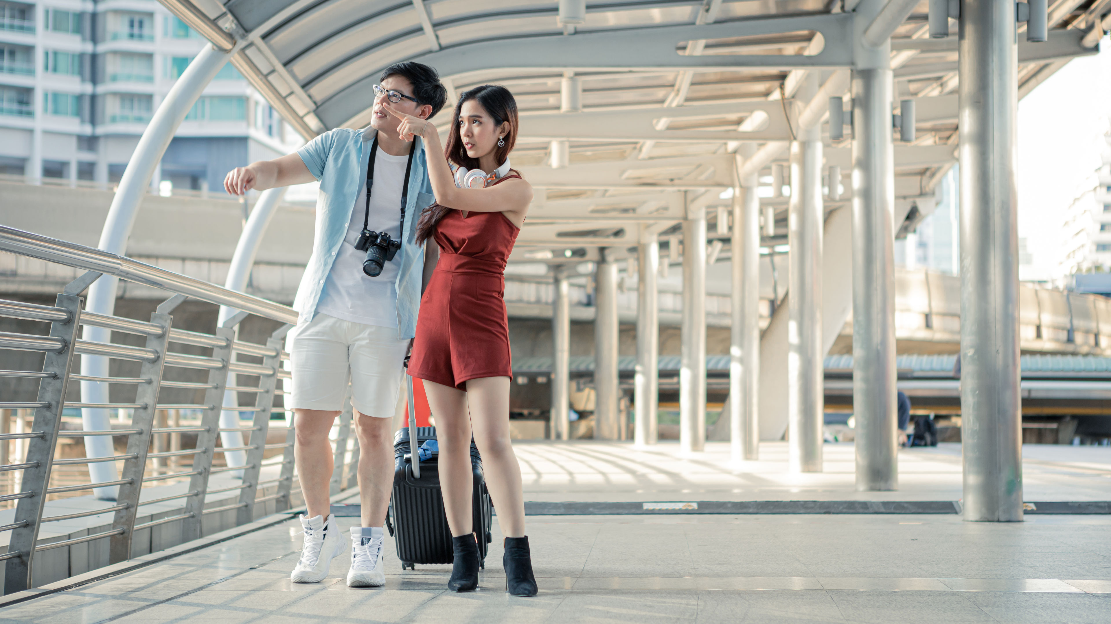 A young couple is dragging a suitcase and talking while travelling around the city.