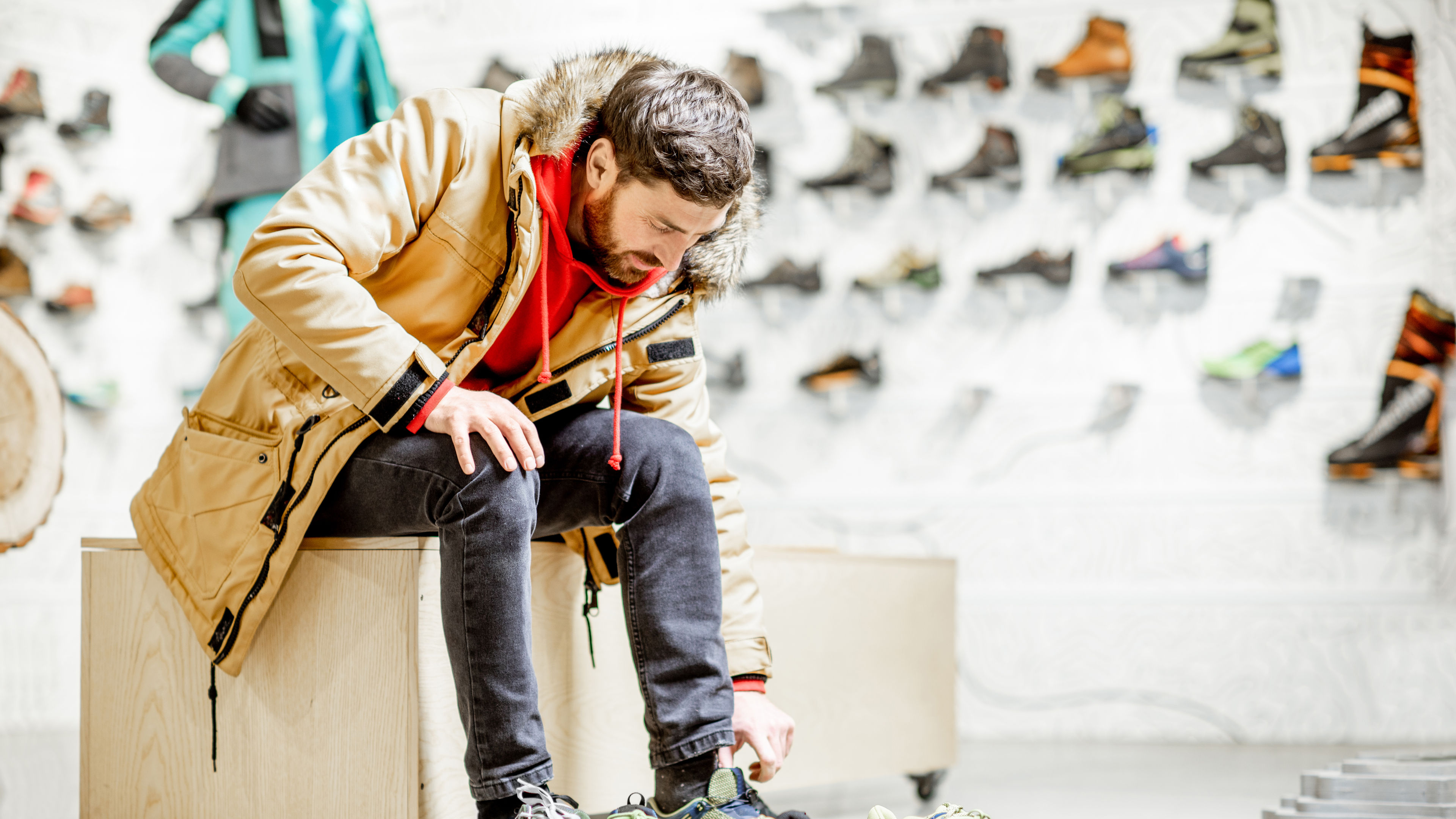 Un hombre, vestido con ropa de abrigo, se sienta en una tienda probándose zapatos.